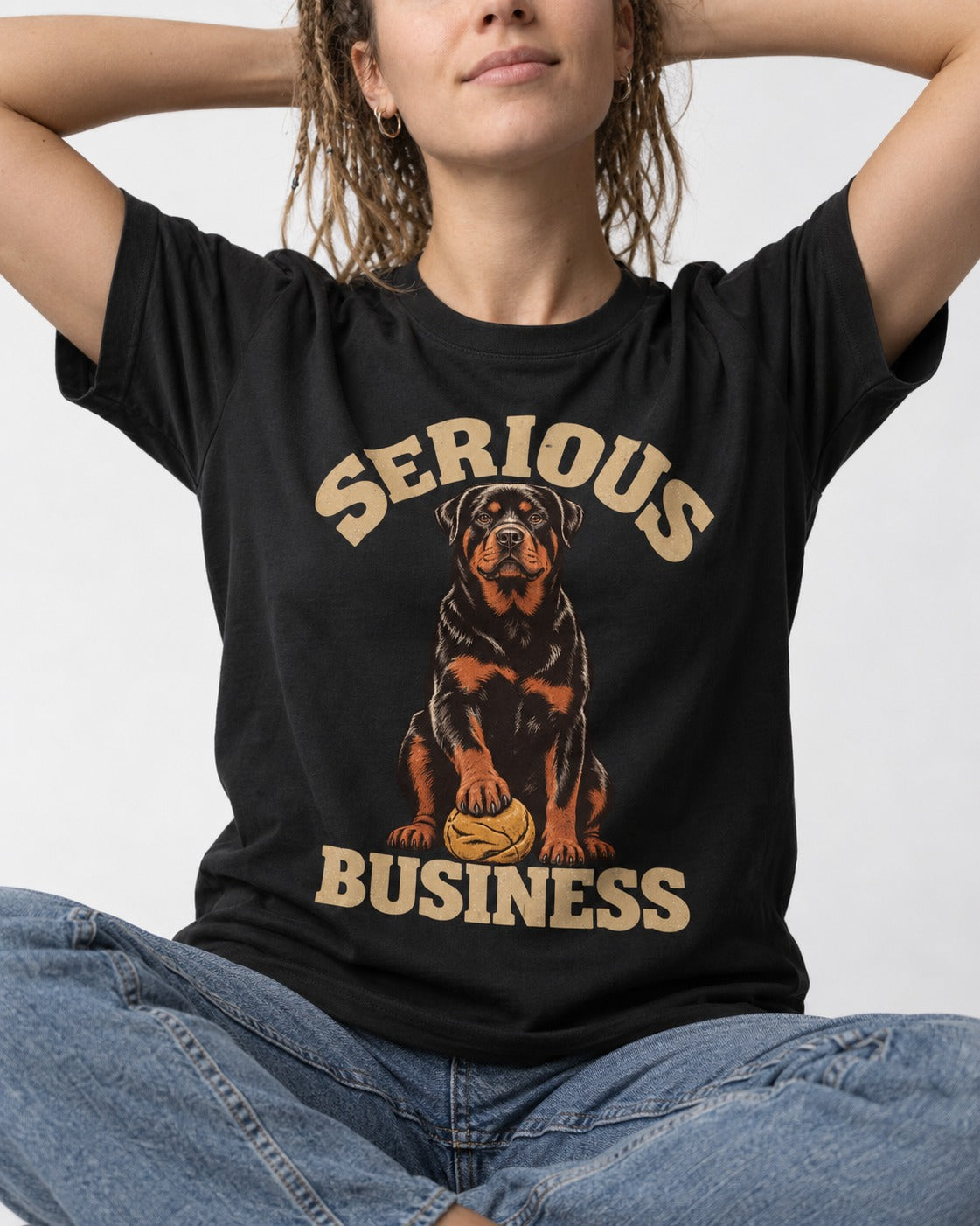 Rottweiler Serious Business Ball Under Paw Graphic T-Shirt in Black, worn by a seated model