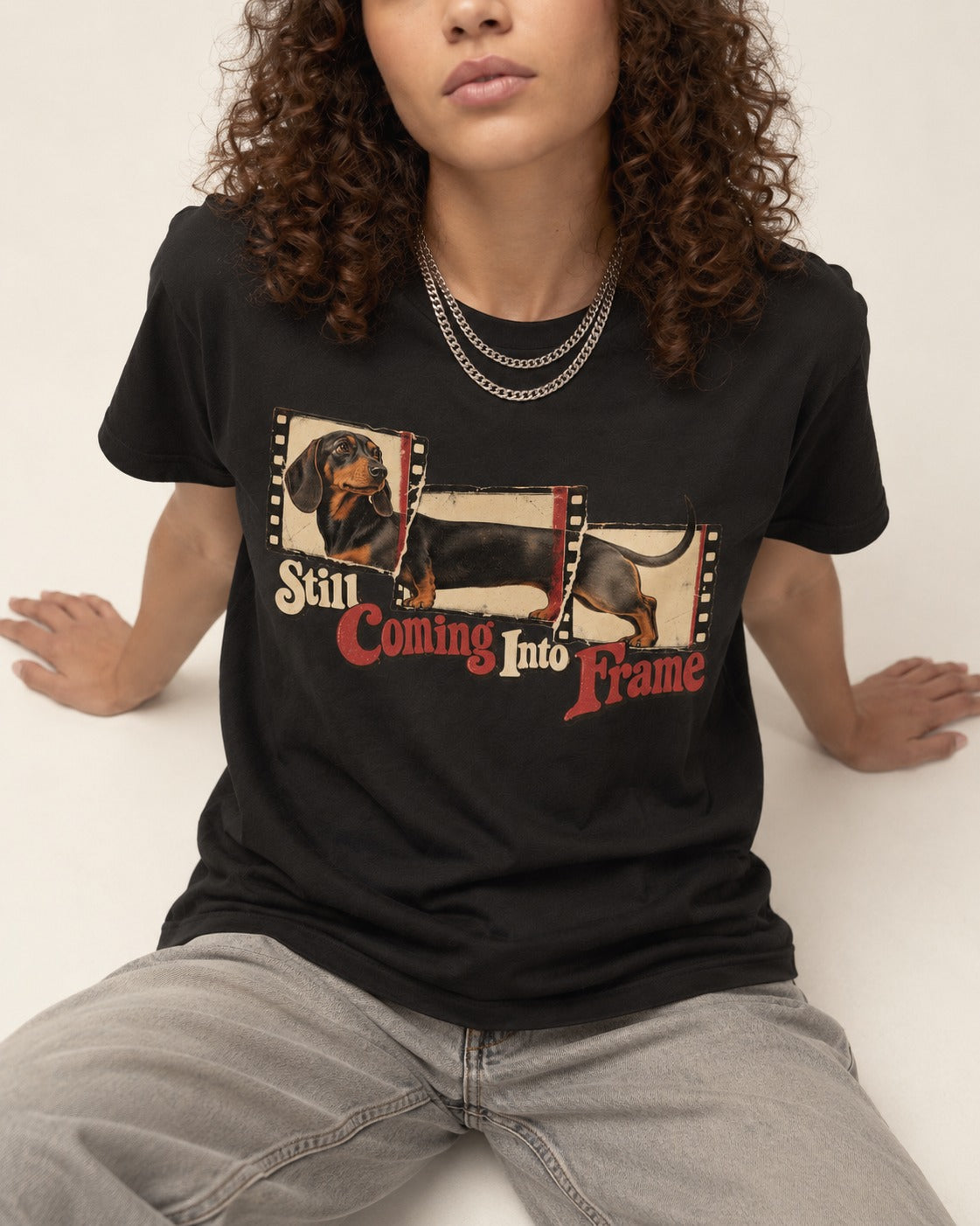 Dachshund Still Coming Into Frame Vintage Filmstrip Graphic T-Shirt in Black, worn by a seated model