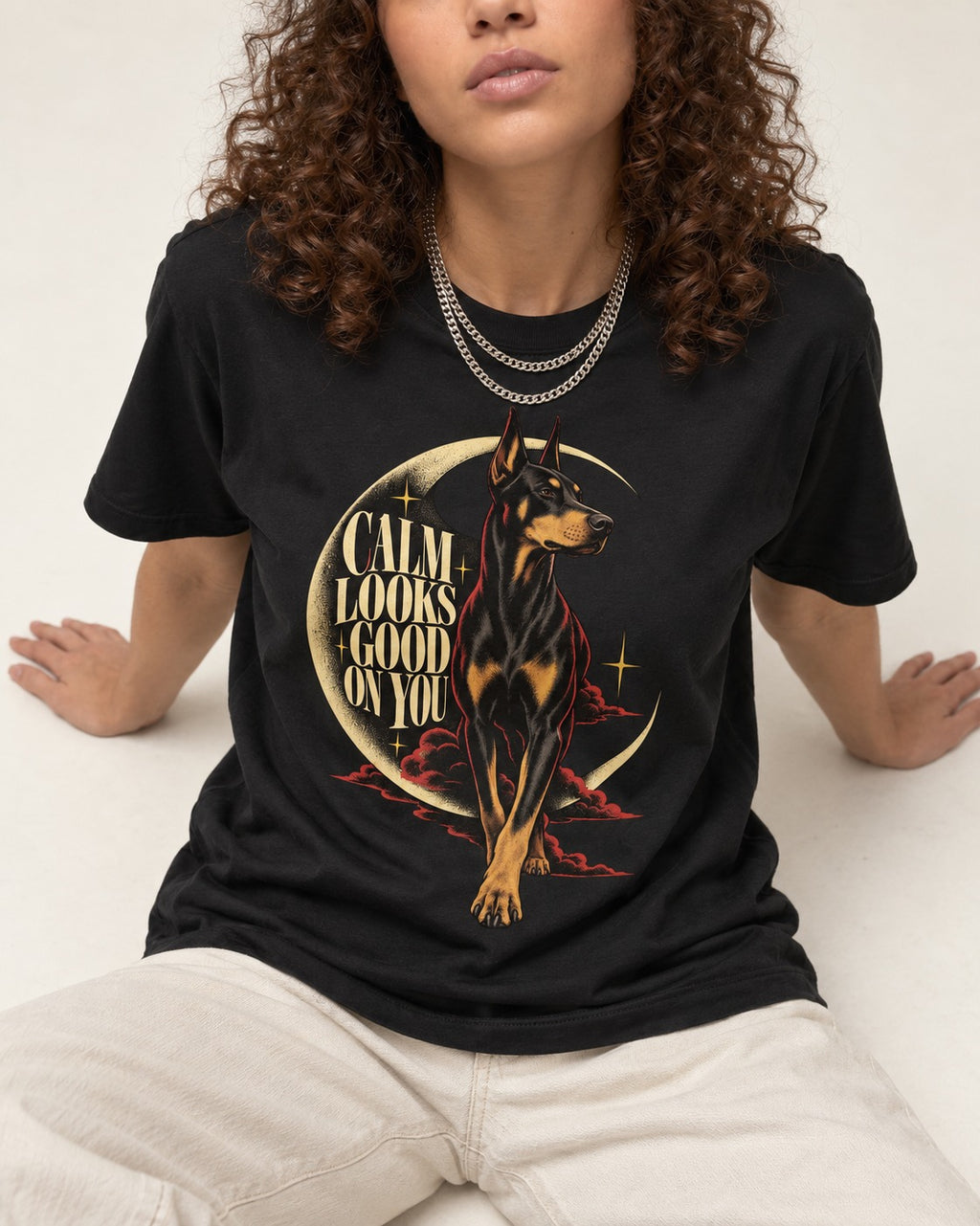 Doberman Calm Looks Good on You Crescent Graphic T-Shirt in Black, worn by a seated model