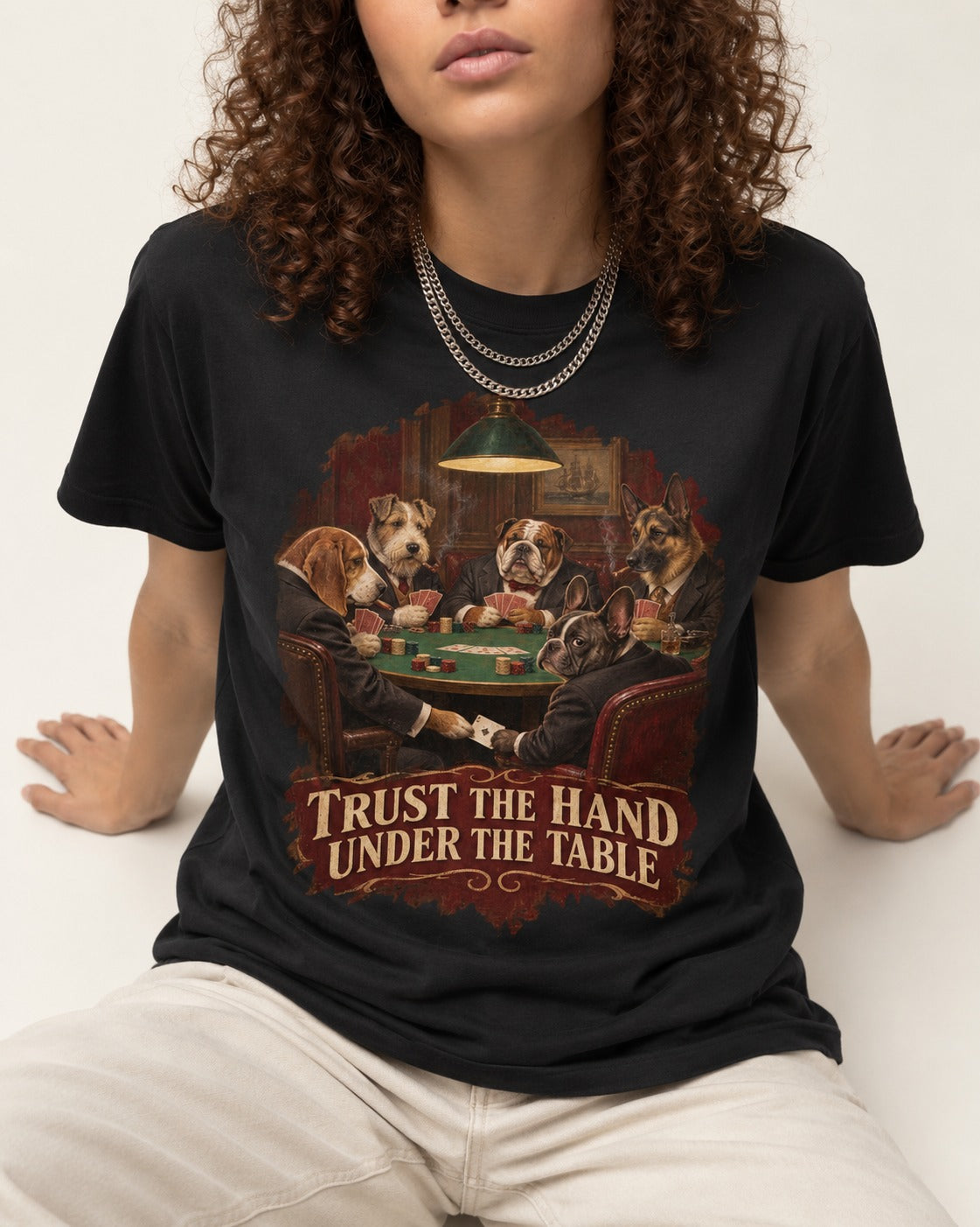 Frenchie Trust the Hand Under the Table Poker Dogs Graphic T-Shirt in Black, worn by a seated model