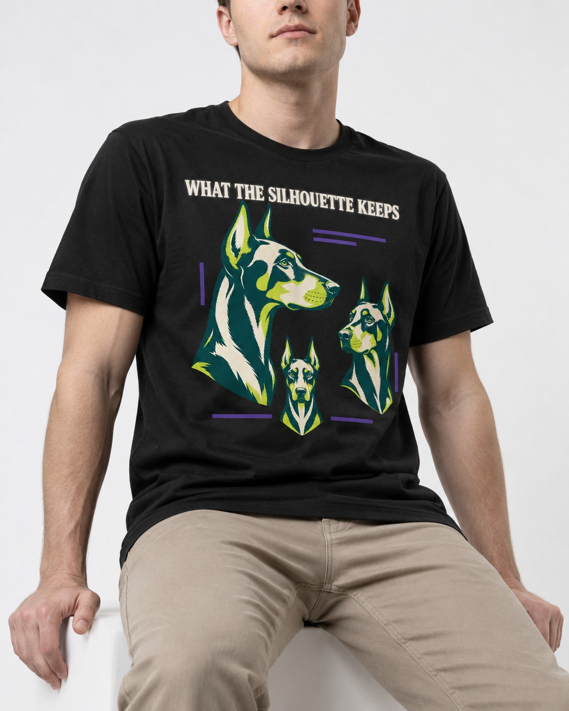 Doberman What the Silhouette Keeps Three Portrait Graphic T-Shirt in Black, worn by a seated model