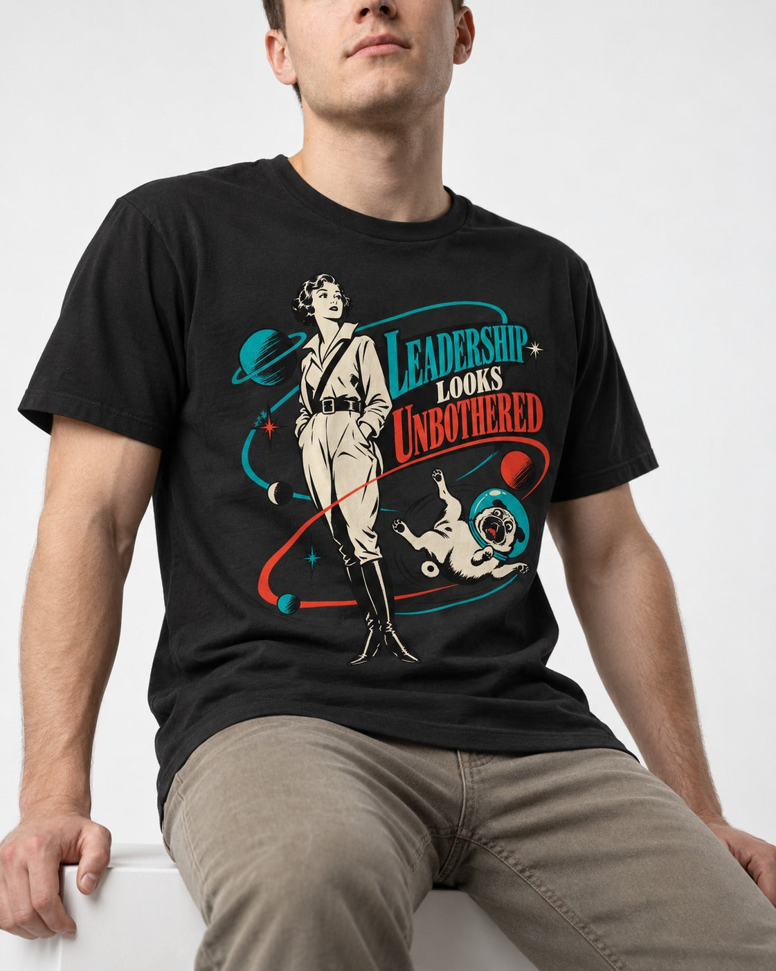 Pug Leadership Looks Unbothered Space Graphic T-Shirt in Black, worn by a seated model
