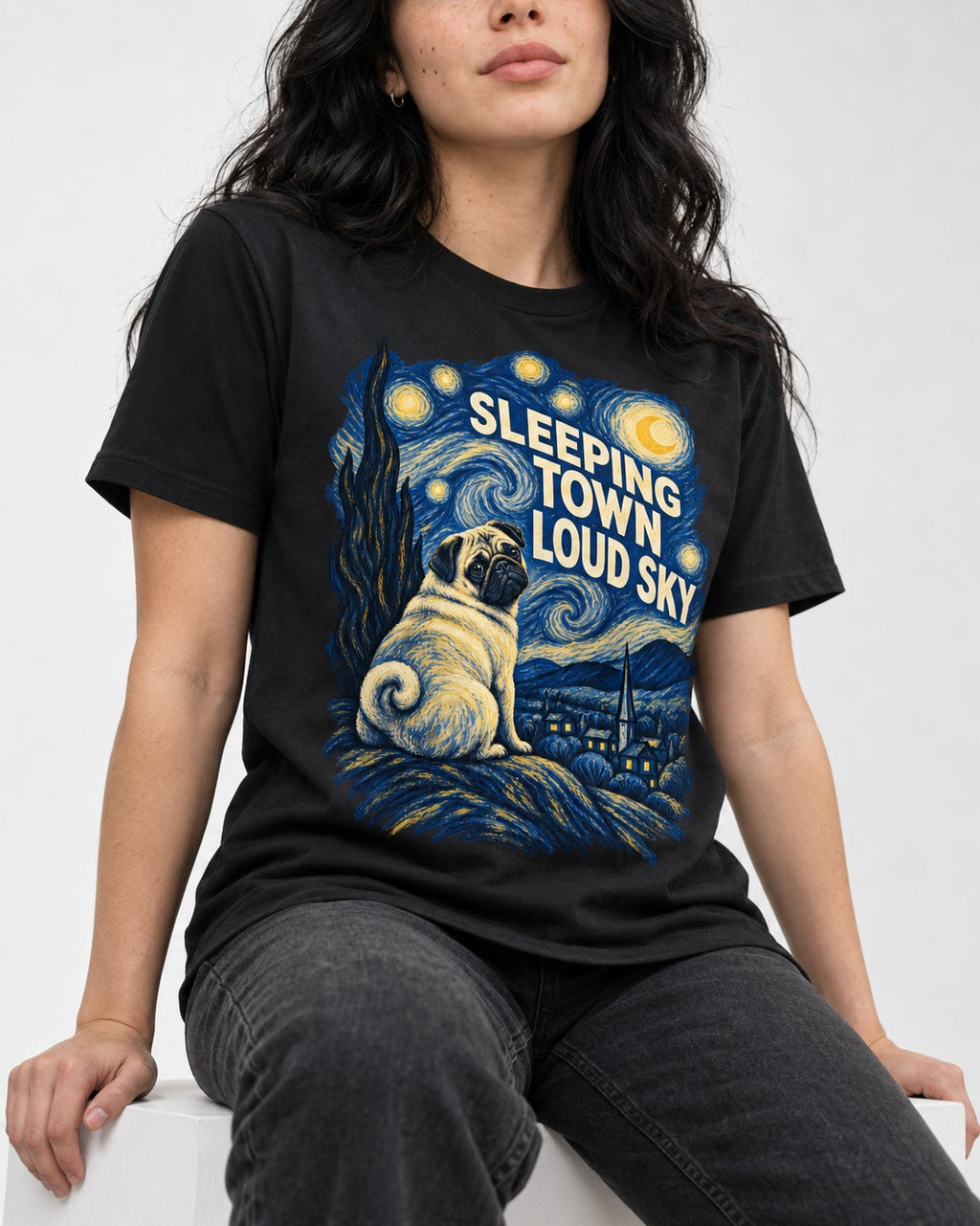 Pug Sleeping Town Loud Sky Starry Night Graphic T-Shirt in Black, worn by a seated model