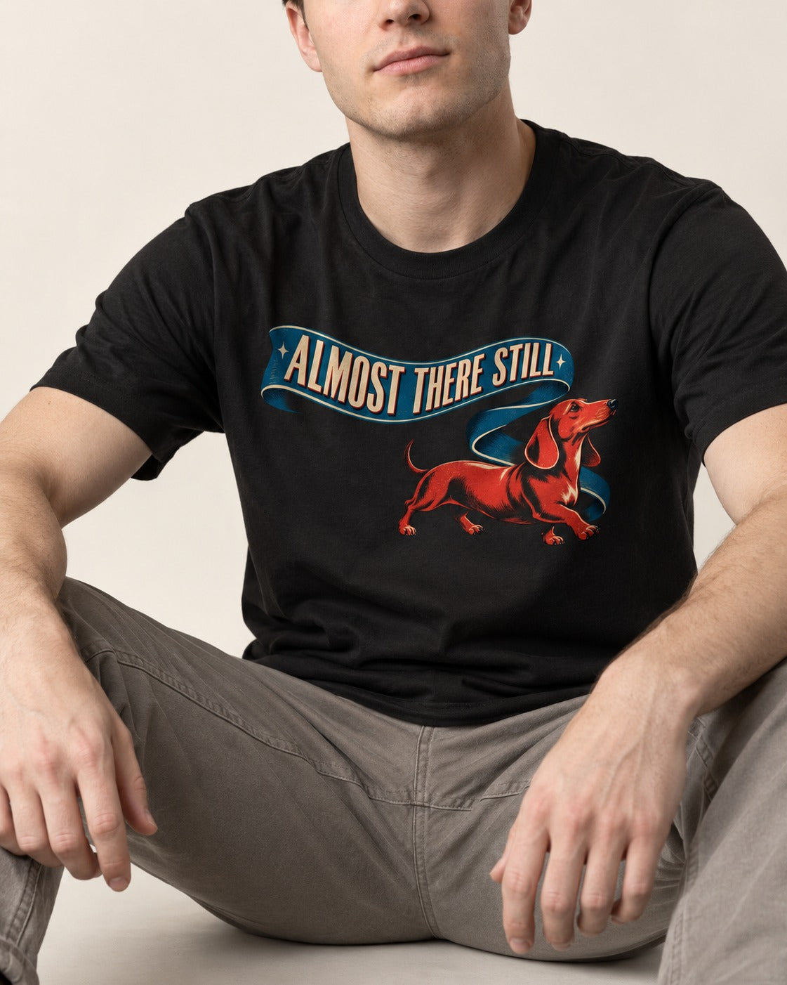 Dachshund Almost There Still Ribbon Graphic T-Shirt in Black, worn by a seated model