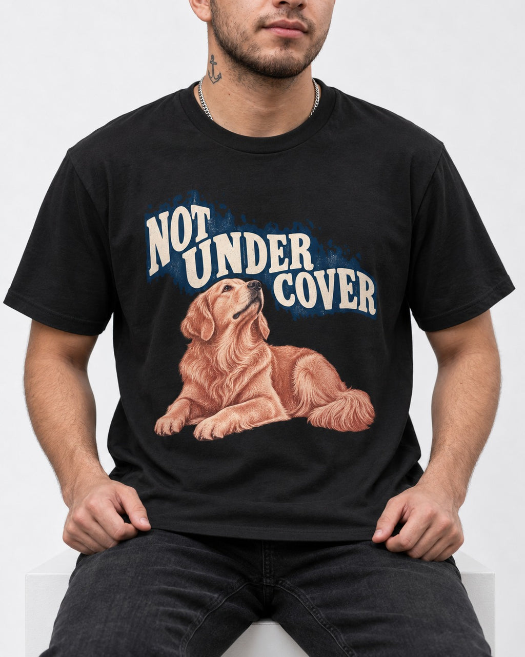 Not Under Cover Reclining Golden Retriever Graphic T-Shirt in Black, worn by a seated model