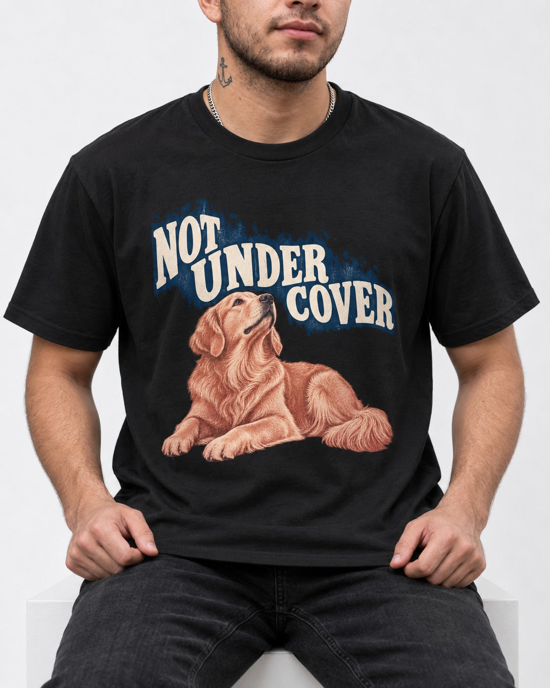 Not Under Cover Reclining Golden Retriever Graphic T-Shirt in Black, worn by a seated model
