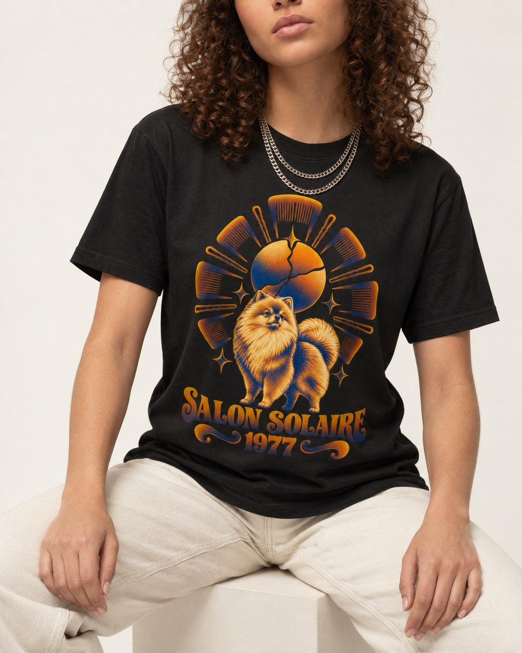 Pomeranian Salon Solaire 1977 Hairbrush Halo Graphic T-Shirt in Black, worn by a seated model