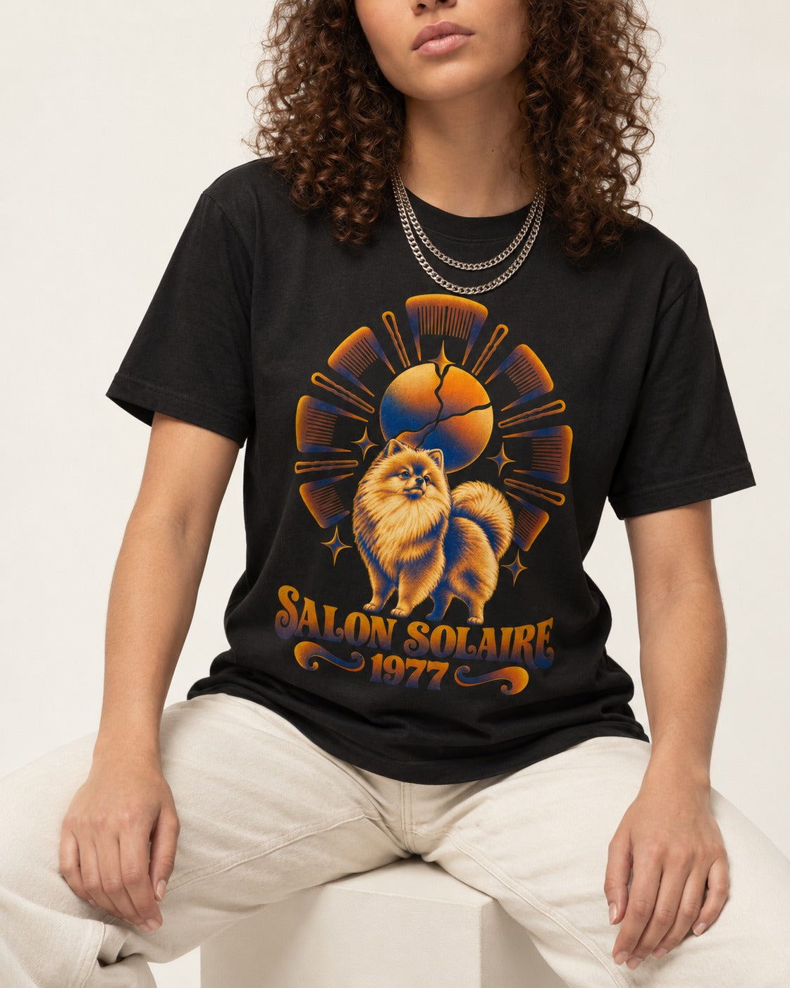 Pomeranian Salon Solaire 1977 Hairbrush Halo Graphic T-Shirt in Black, worn by a seated model