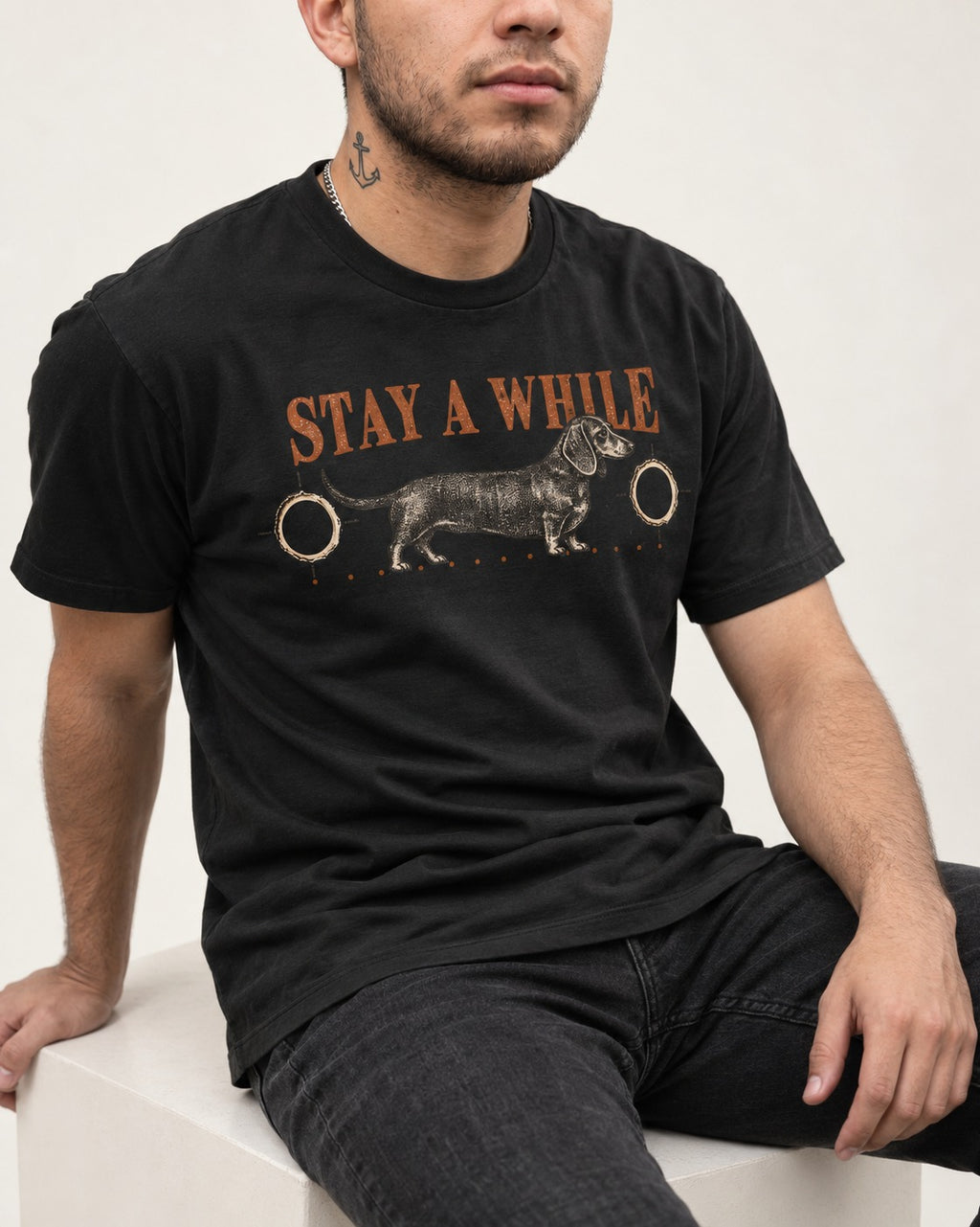 Dachshund Stay A While Ornamental Portrait Graphic T-Shirt in Black, worn by a seated model