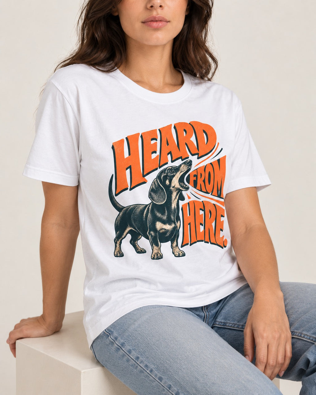 Dachshund Heard From Here T-Shirt in White, worn by a seated model