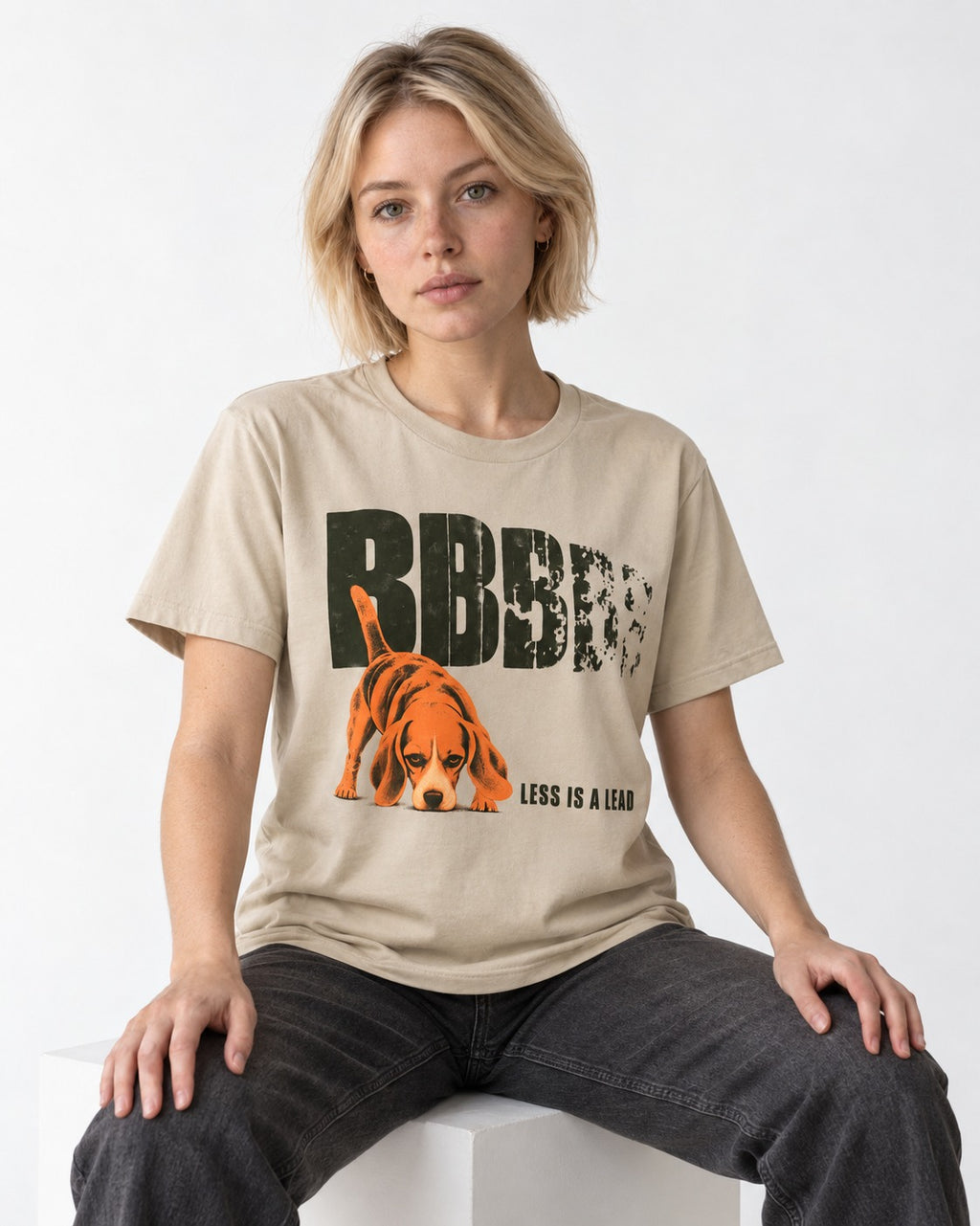 Less Is a Lead Beagle T-Shirt in Sand, worn by a seated model
