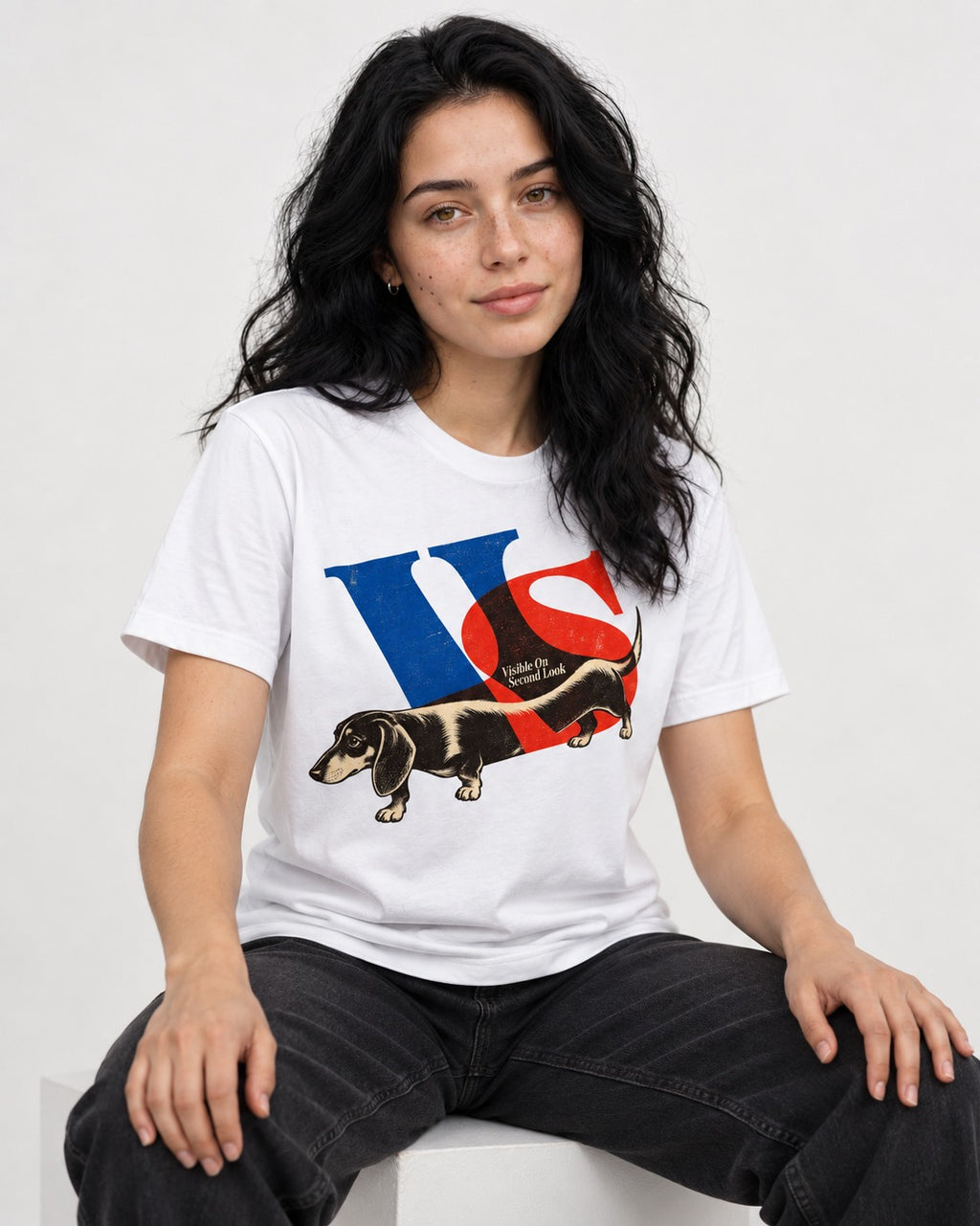 Dachshund VS Visible On Second Look Graphic T-Shirt in White, worn by a seated model