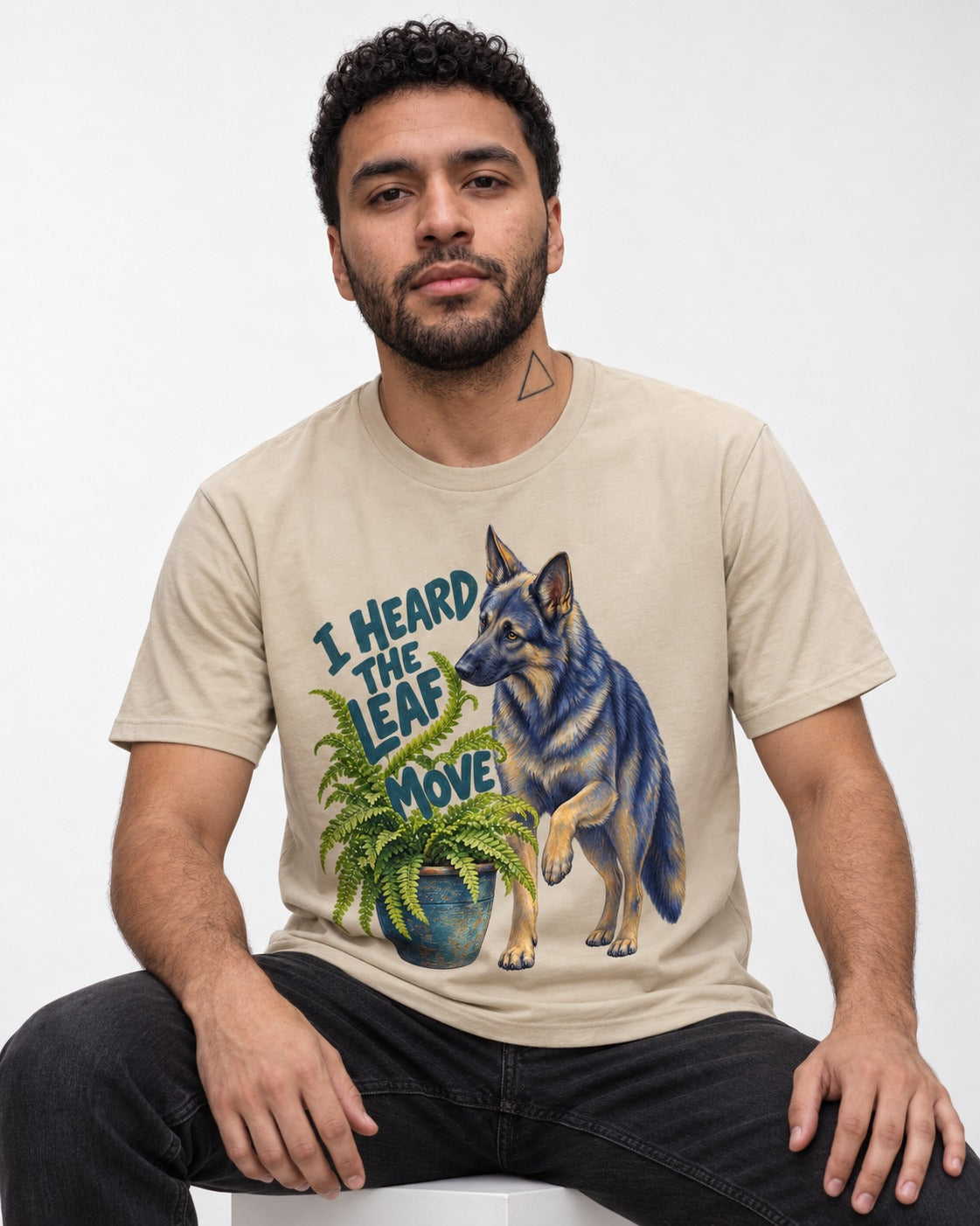 German Shepherd Dog Heard the Leaf Move T-Shirt in Sand, worn by a seated model
