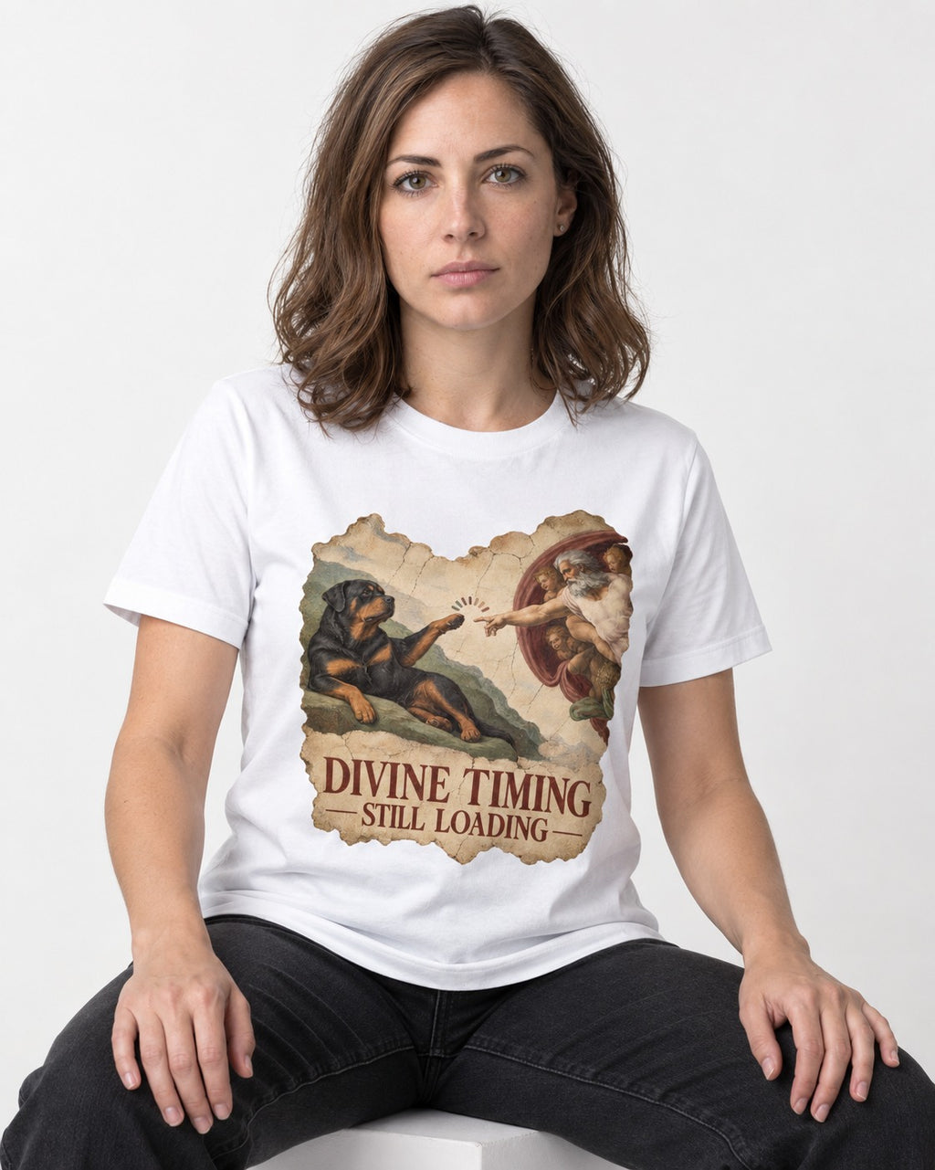 Rottweiler Divine Timing Still Loading Creation Parody Graphic T-Shirt in White, worn by a seated model
