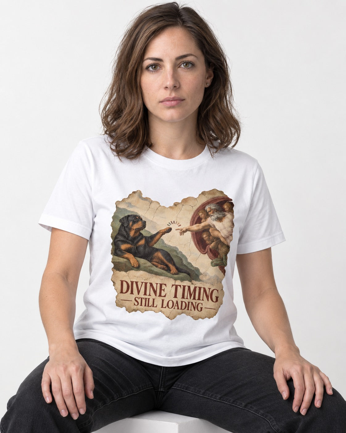Rottweiler Divine Timing Still Loading Creation Parody Graphic T-Shirt in White, worn by a seated model