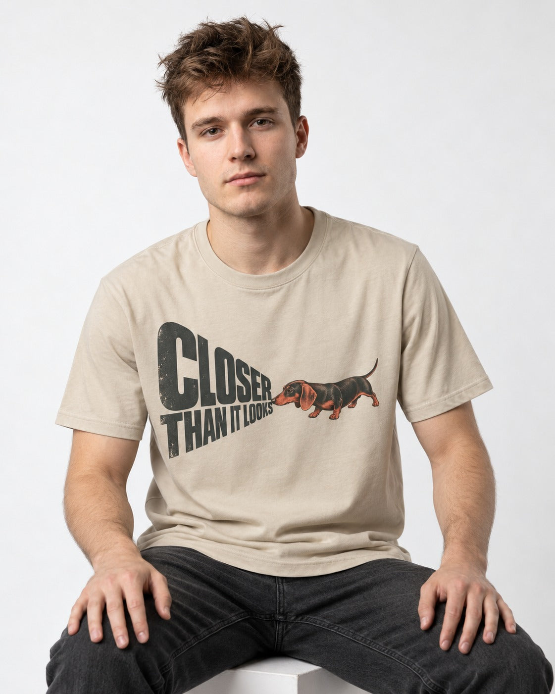 Dachshund Closer Than It Looks T-Shirt in Sand, worn by a seated model
