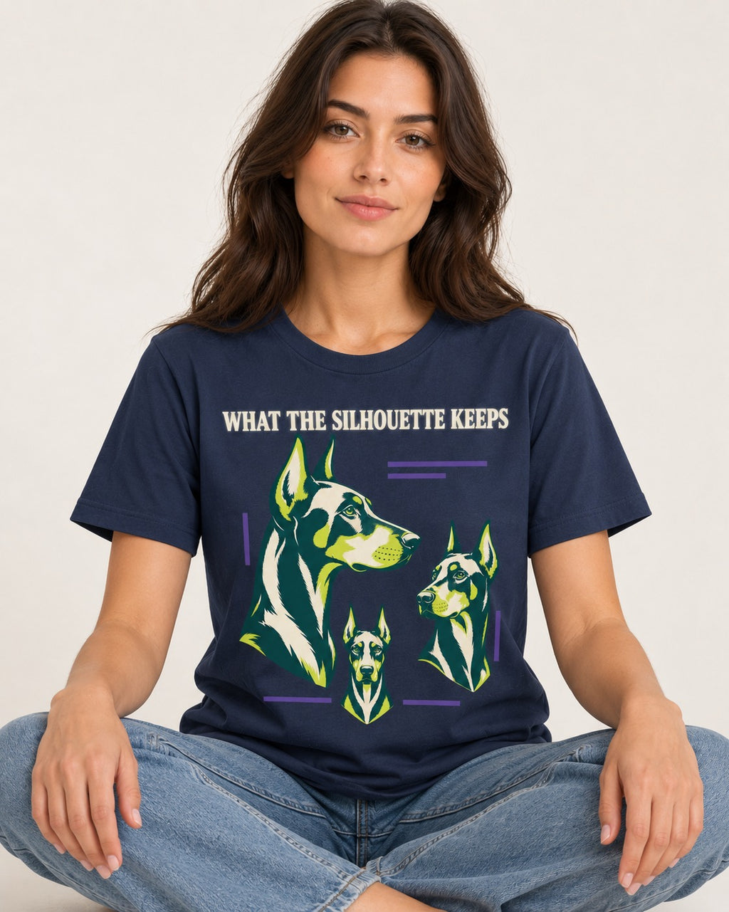 Doberman What the Silhouette Keeps Three Portrait Graphic T-Shirt in Navy, worn by a seated model