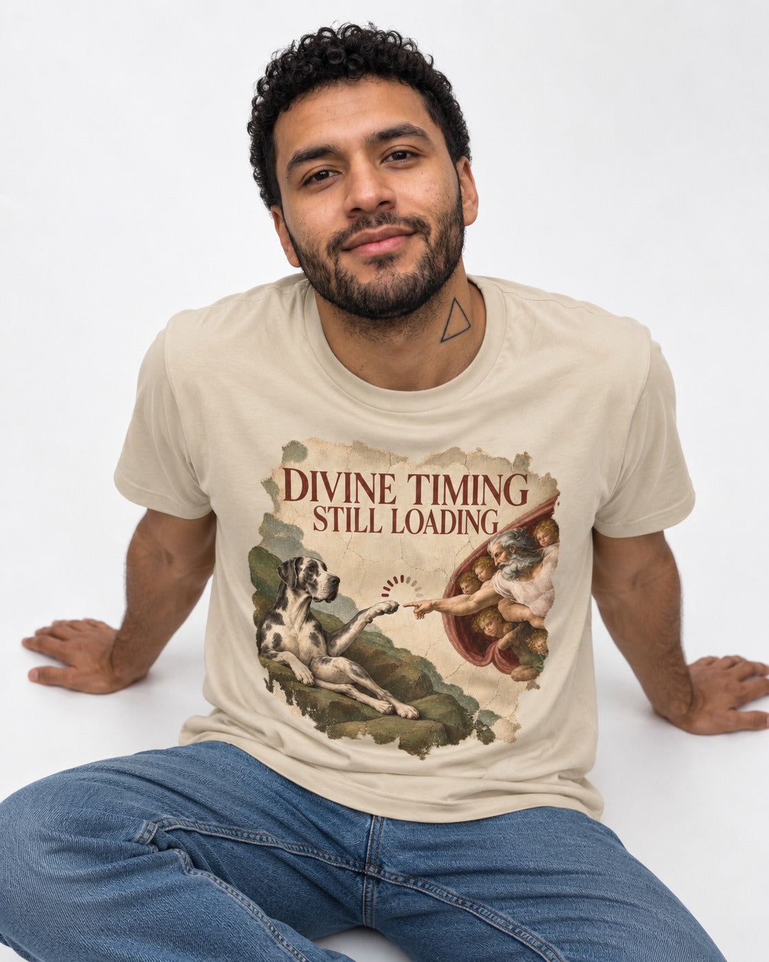 Great Dane Divine Timing Still Loading T-Shirt in Sand, worn by a seated model