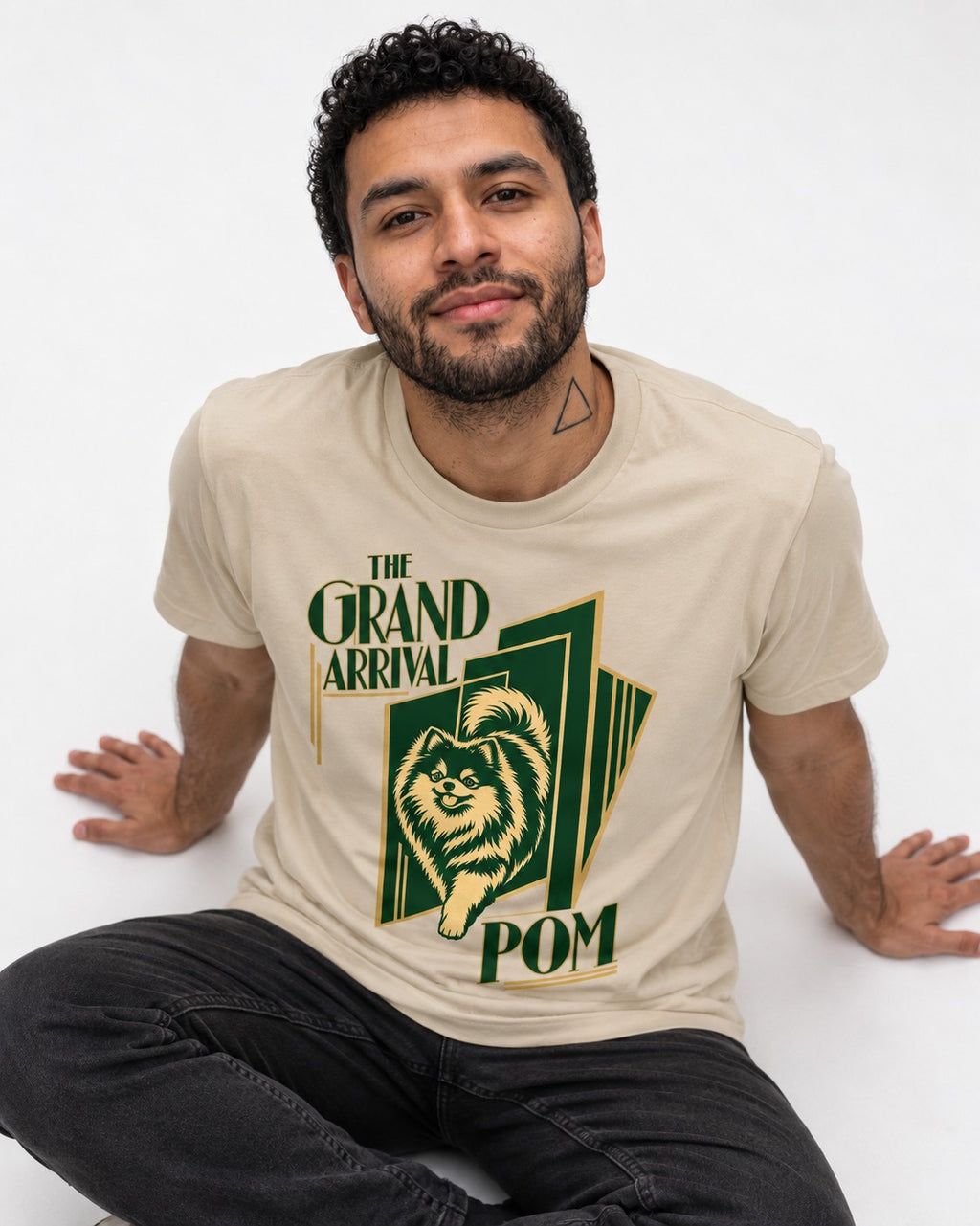 The Grand Arrival Pomeranian T-Shirt in Sand, worn by a seated model