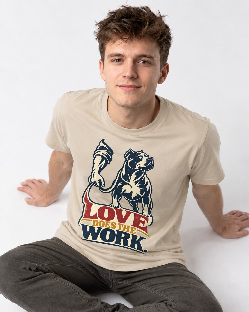 Pitbull Love Does the Work T-Shirt in Sand, worn by a seated model