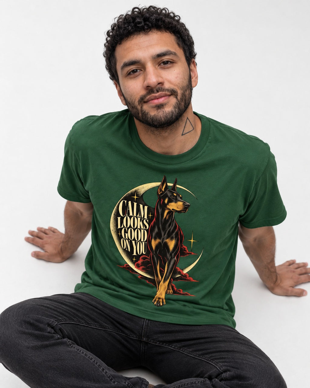 Doberman Calm Looks Good on You Crescent Graphic T-Shirt in Forest Green, worn by a seated model