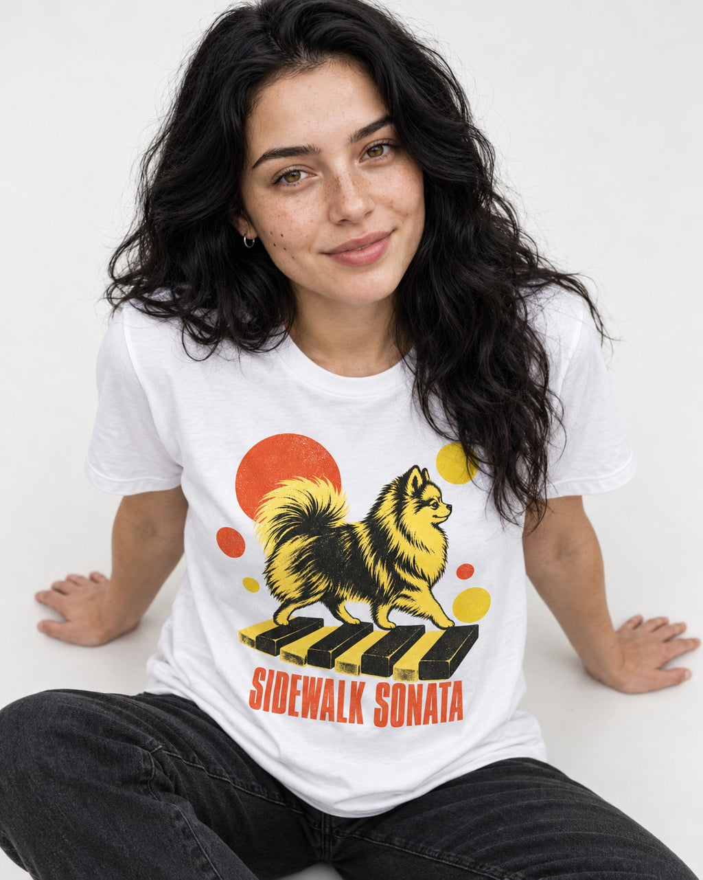 Pomeranian Sidewalk Sonata Piano Graphic T-Shirt in White, worn by a seated model