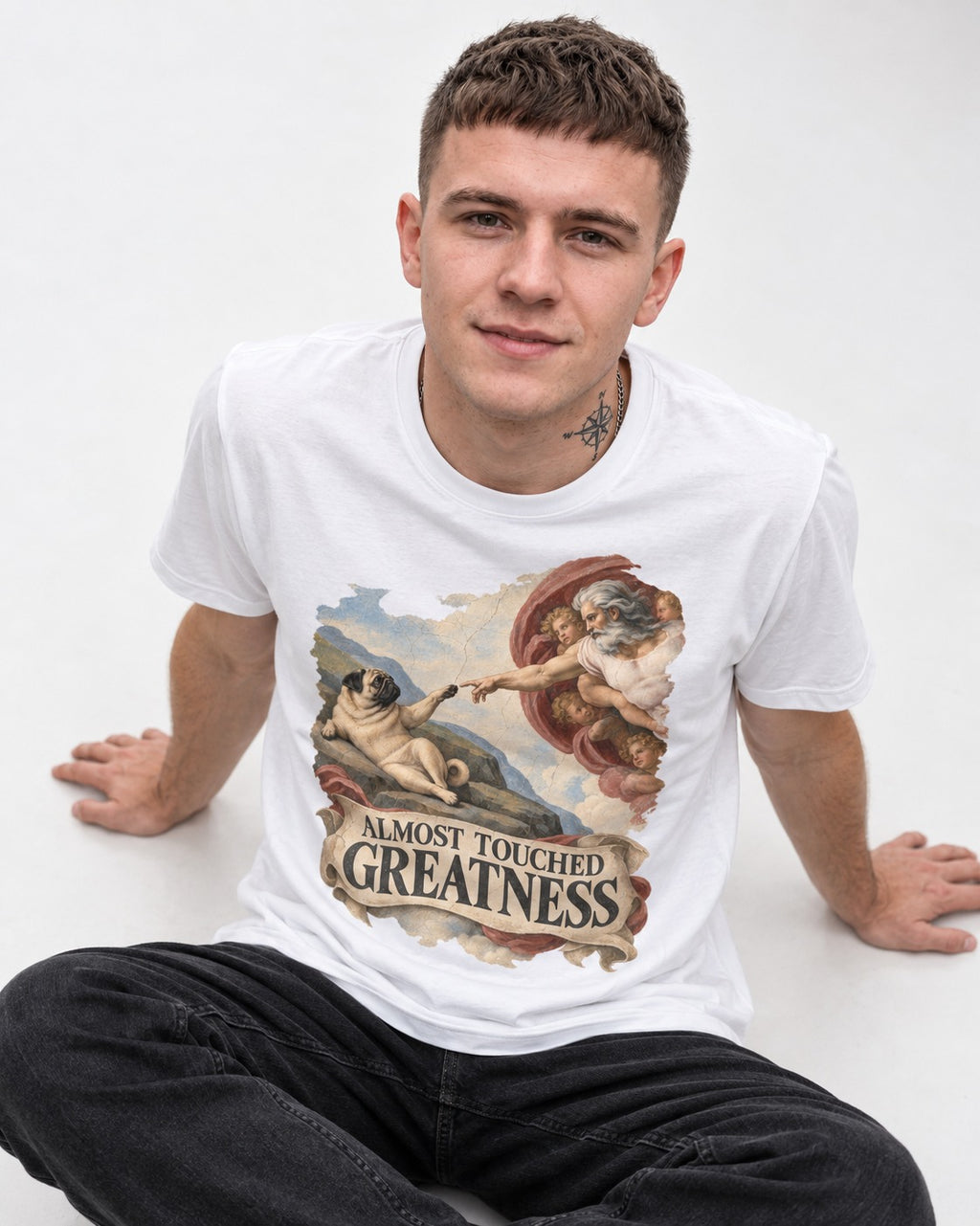 Pug Almost Touched Greatness Creation Parody Graphic T-Shirt in White, worn by a seated model