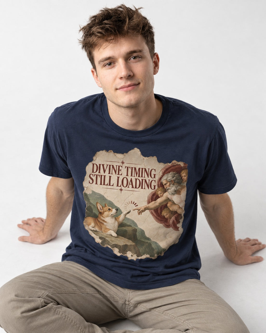 Corgi Divine Timing Still Loading Creation Parody T-Shirt in Navy, worn by a seated model