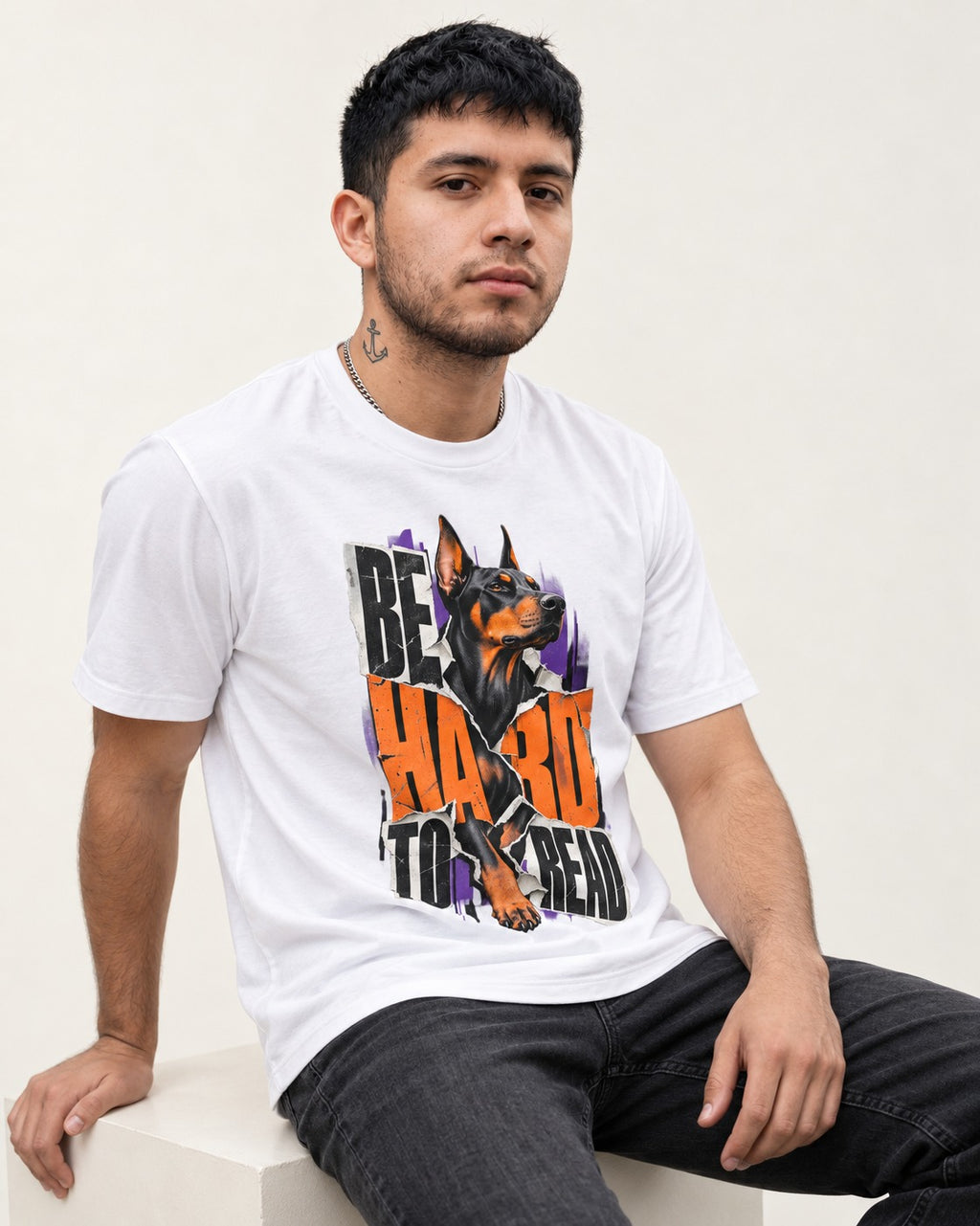 Doberman Be Hard to Read Torn Poster Graphic T-Shirt in White, worn by a seated model