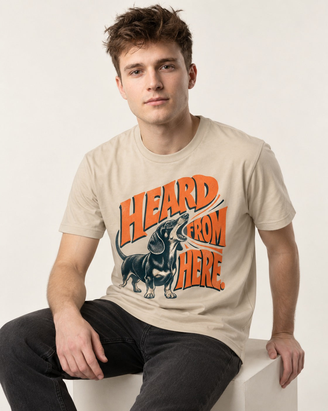 Dachshund Heard From Here T-Shirt in Sand, worn by a seated model