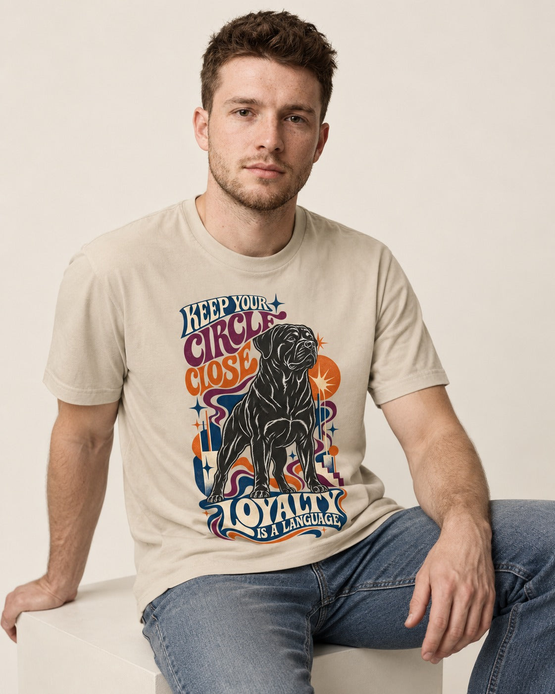 Keep Your Rottweiler Circle Close T-Shirt in Sand, worn by a seated model