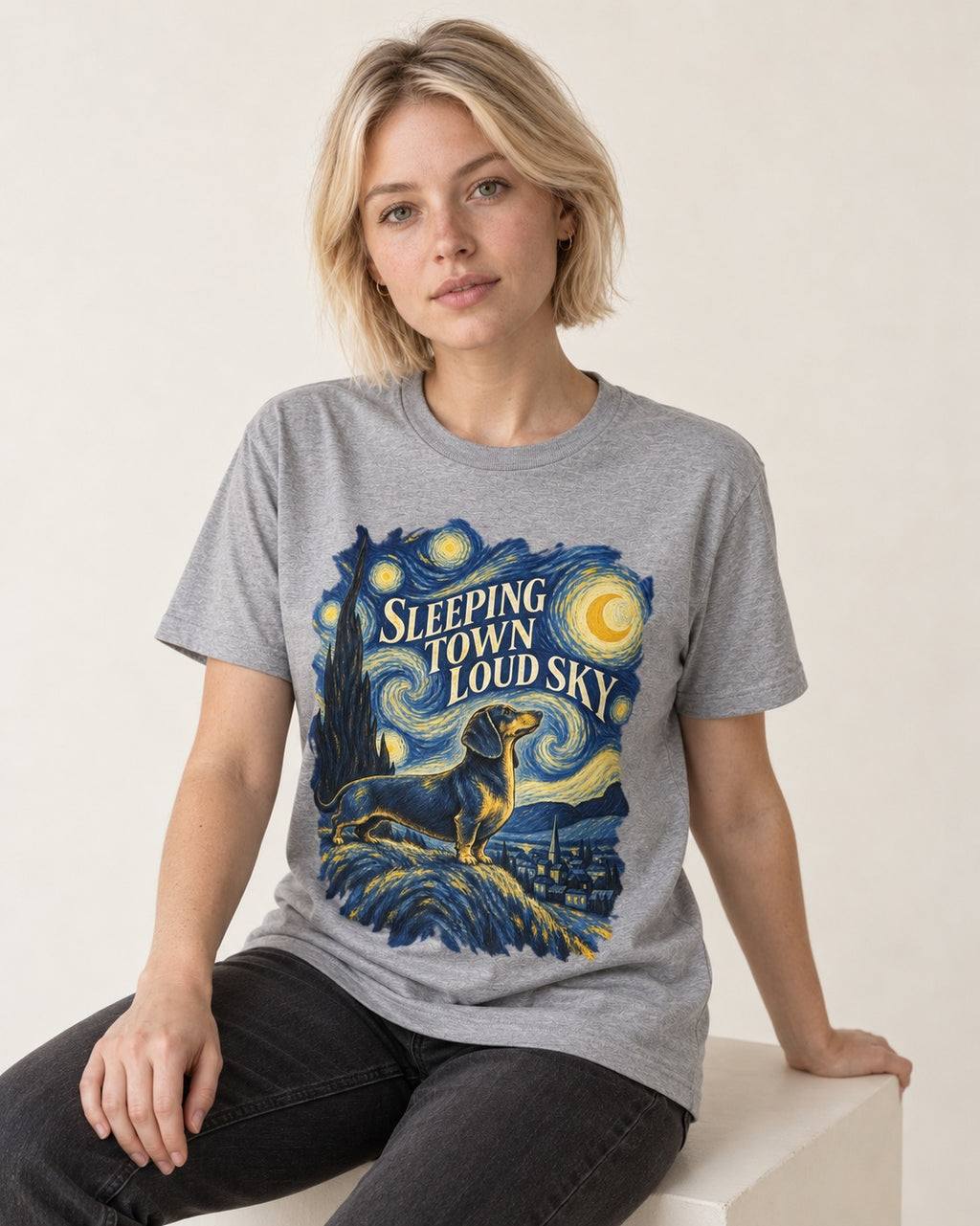 Dachshund Sleeping Town Loud Sky Starry Night Graphic T-Shirt in Sport Grey, worn by a seated model