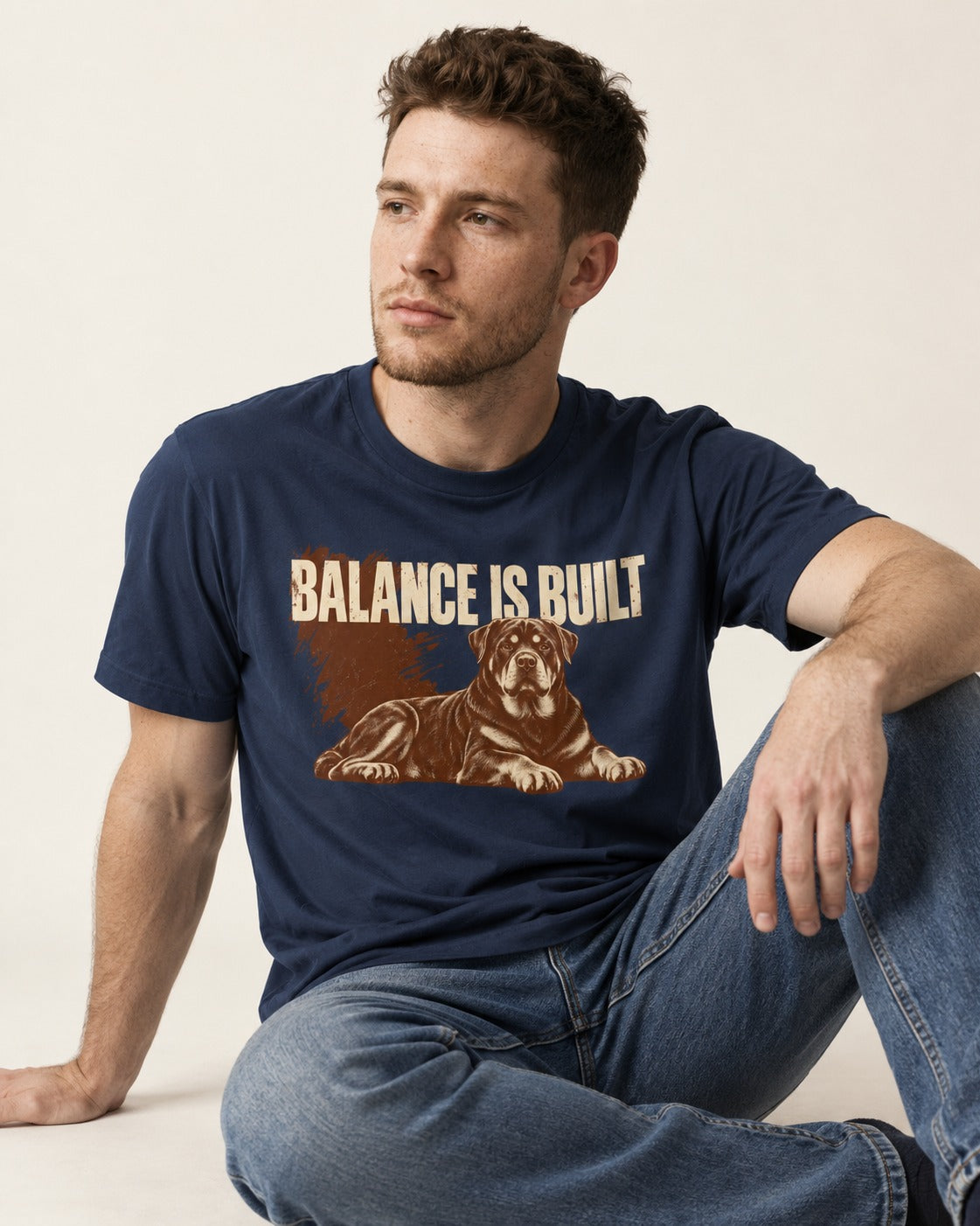 Rottweiler Balance Is Built Resting Strength Graphic T-Shirt in Navy, worn by a seated model