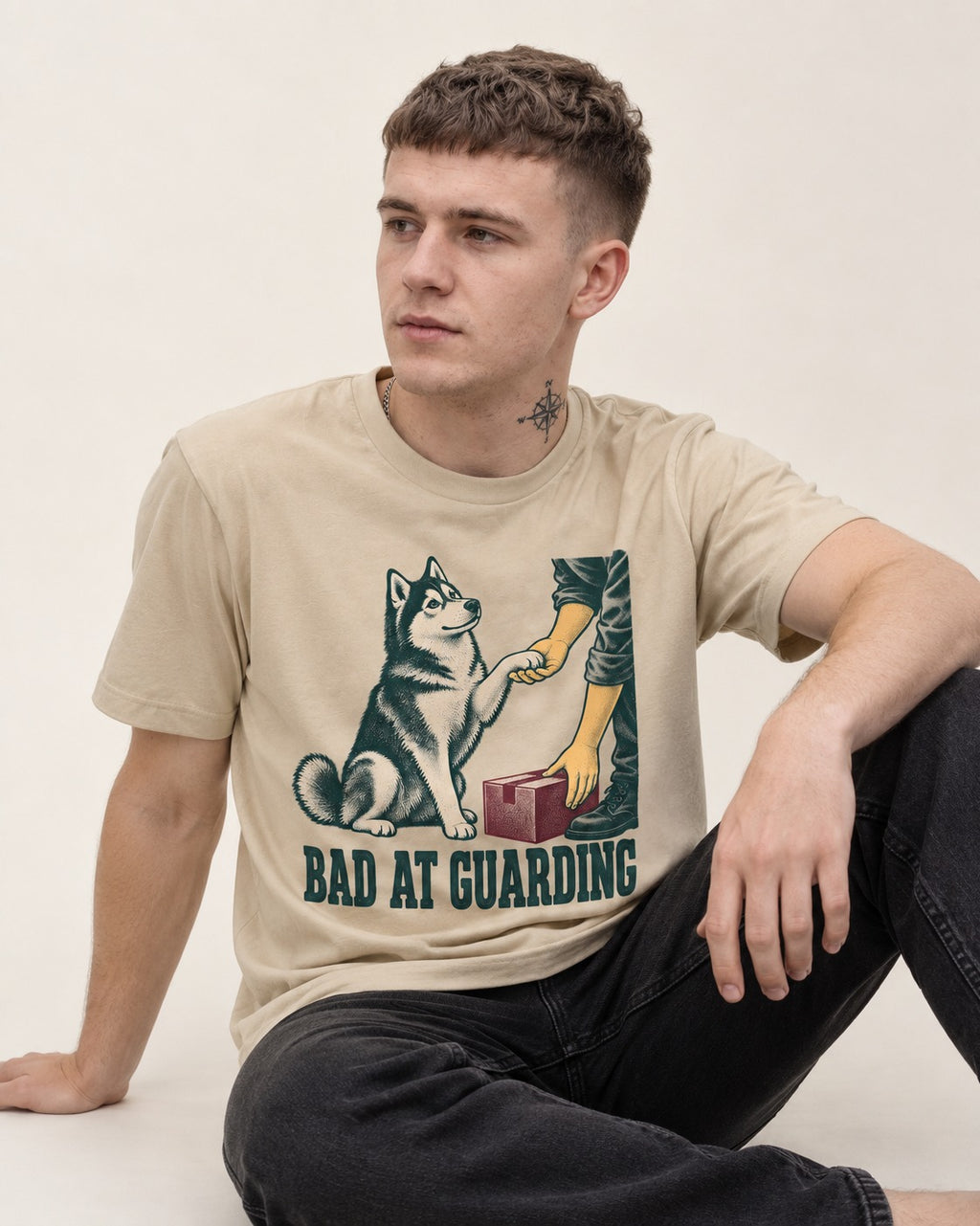 Husky's Bad at Guarding T-Shirt in Sand, worn by a seated model