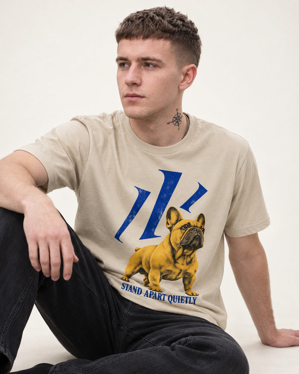 Frenchie Stand Apart Quietly T-Shirt in Sand, worn by a seated model