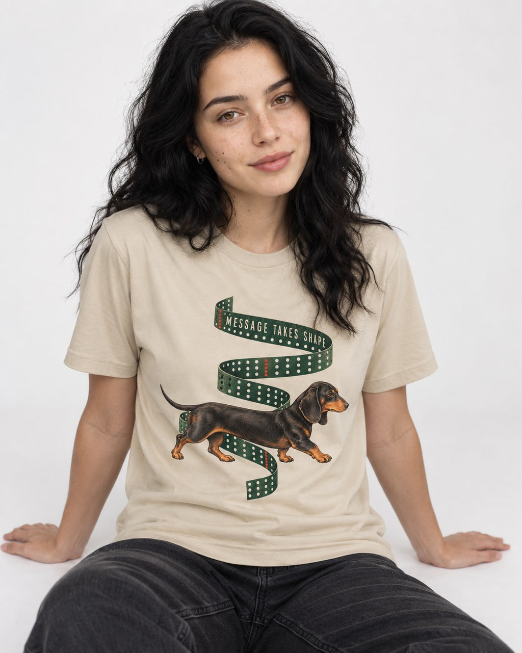 Dachshund Message Takes Shape T-Shirt in Sand, worn by a seated model