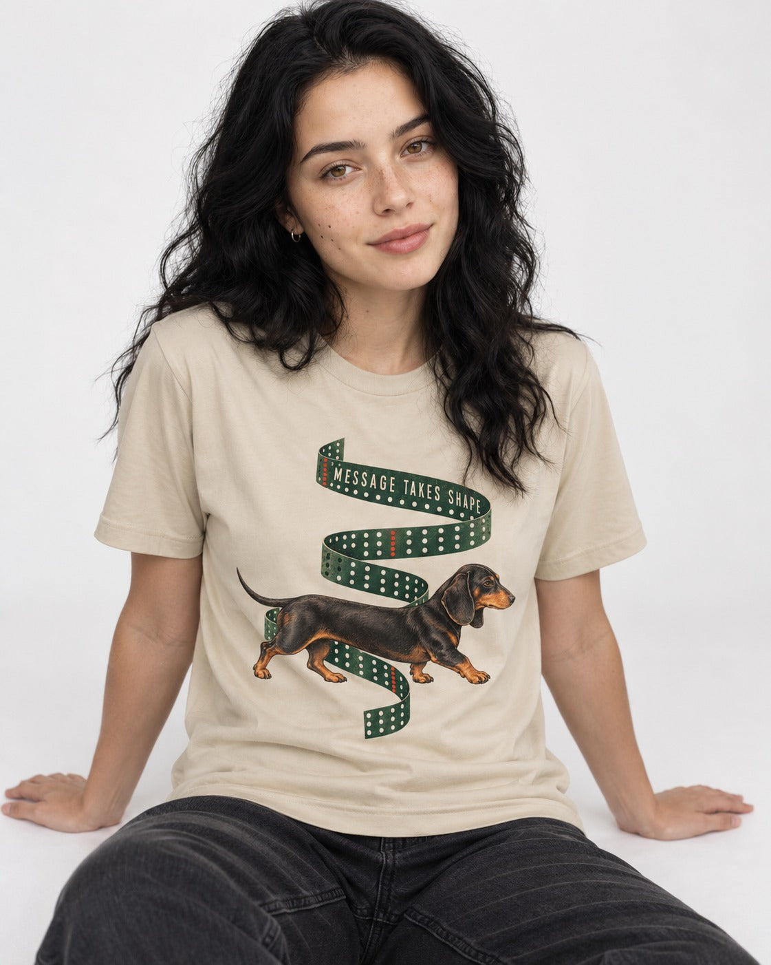 Dachshund Message Takes Shape T-Shirt in Sand, worn by a seated model
