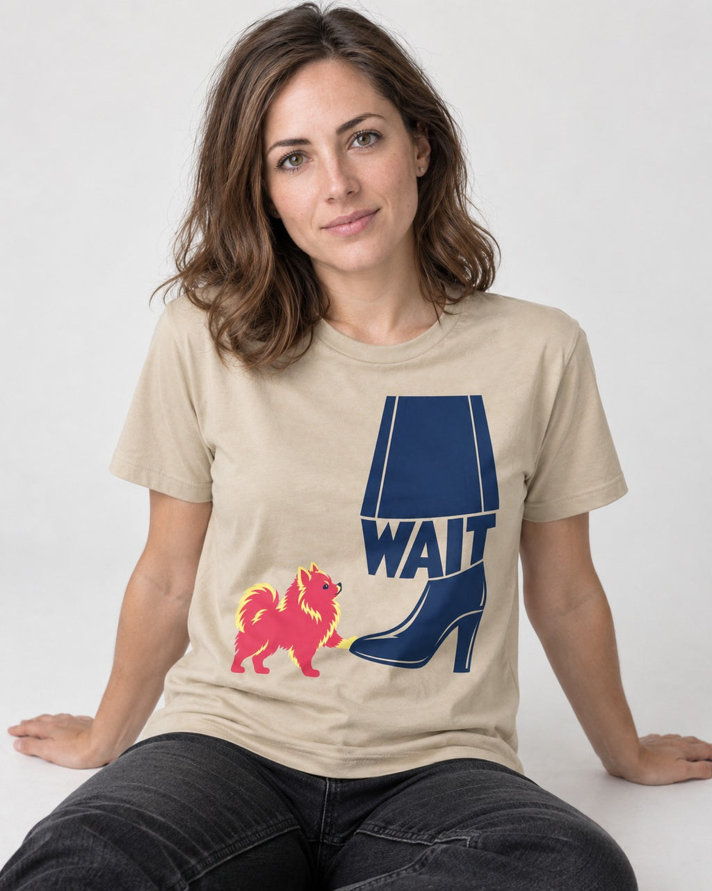 Pomeranian Says Wait T-Shirt in Sand, worn by a seated model