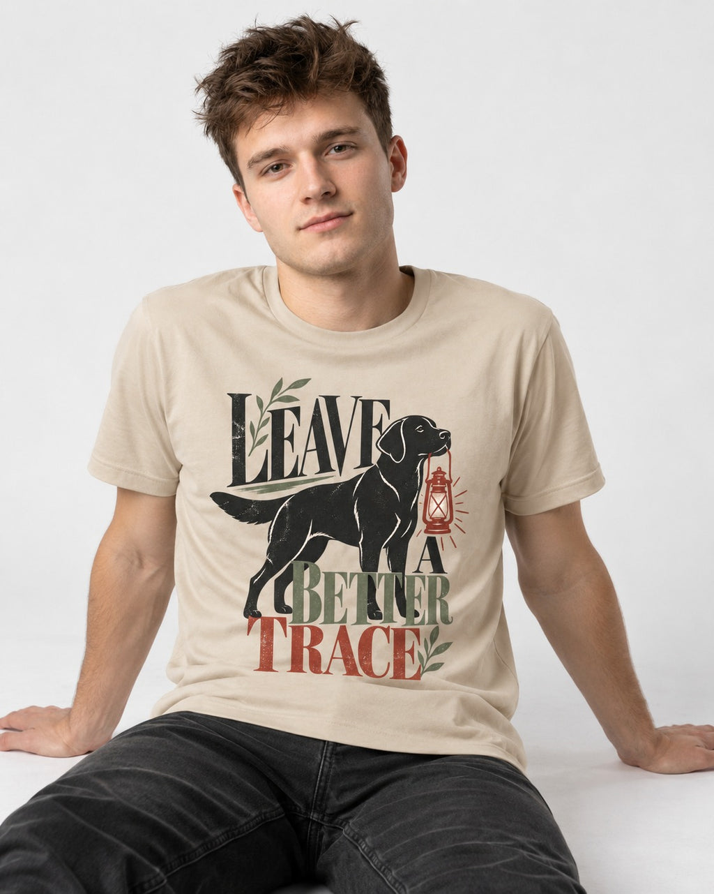Leave a Better Trace Labrador Retriever T-Shirt in Sand, worn by a seated model