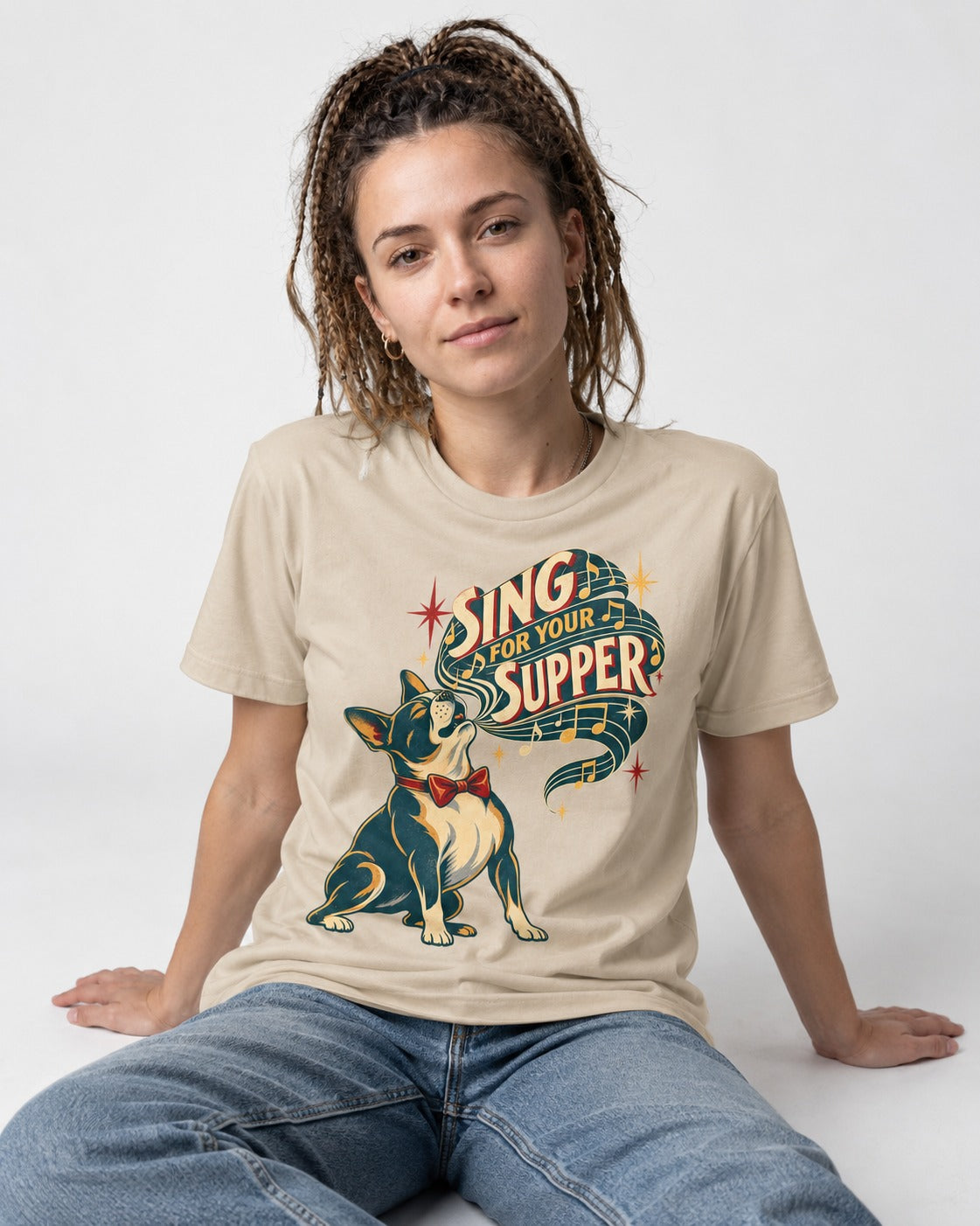 Boston Terrier Sing for Your Supper T-Shirt in Sand, worn by a seated model