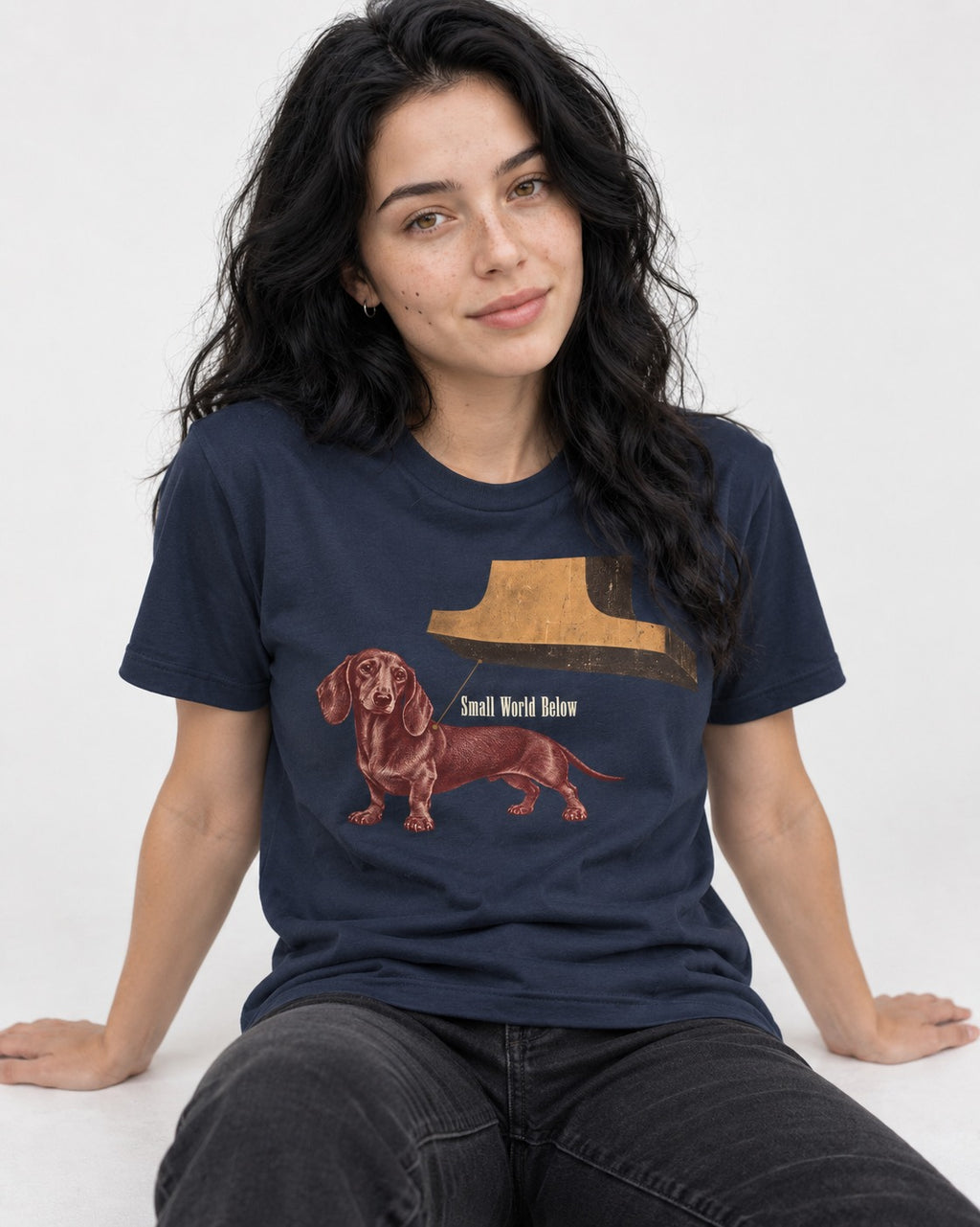 Dachshund Small World Below Giant Shoe Graphic T-Shirt in Navy, worn by a seated model