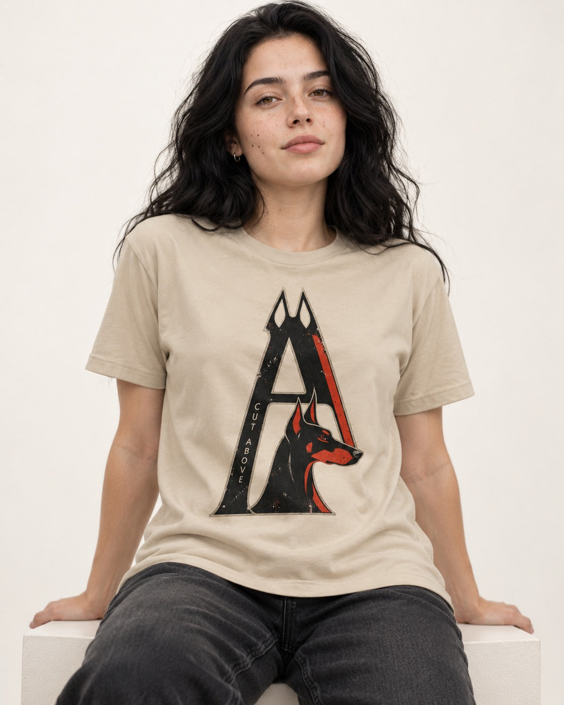Doberman A Cut Above T-Shirt in Sand, worn by a seated model