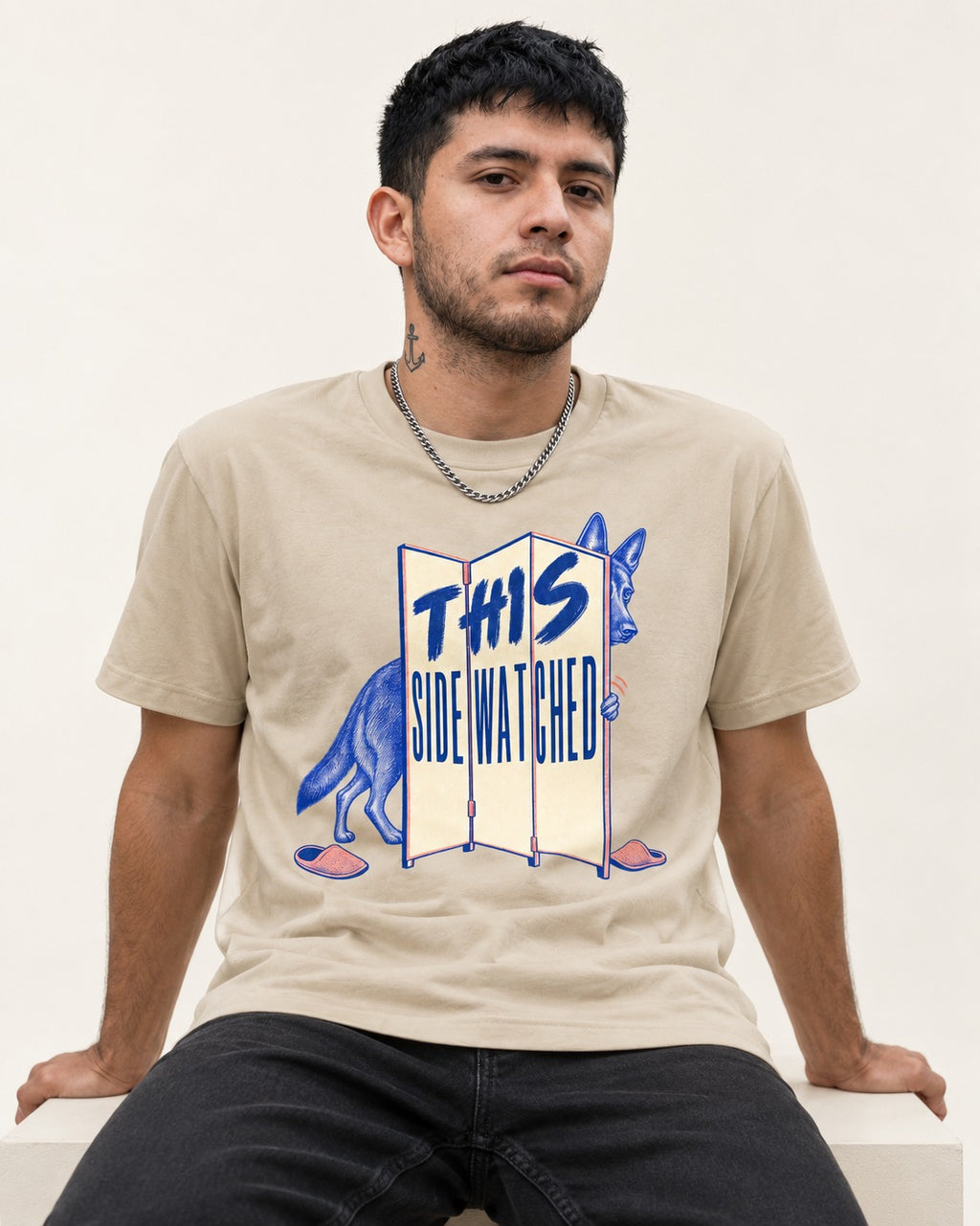 This Side Watched by German Shepherd Dog T-Shirt in Sand, worn by a seated model