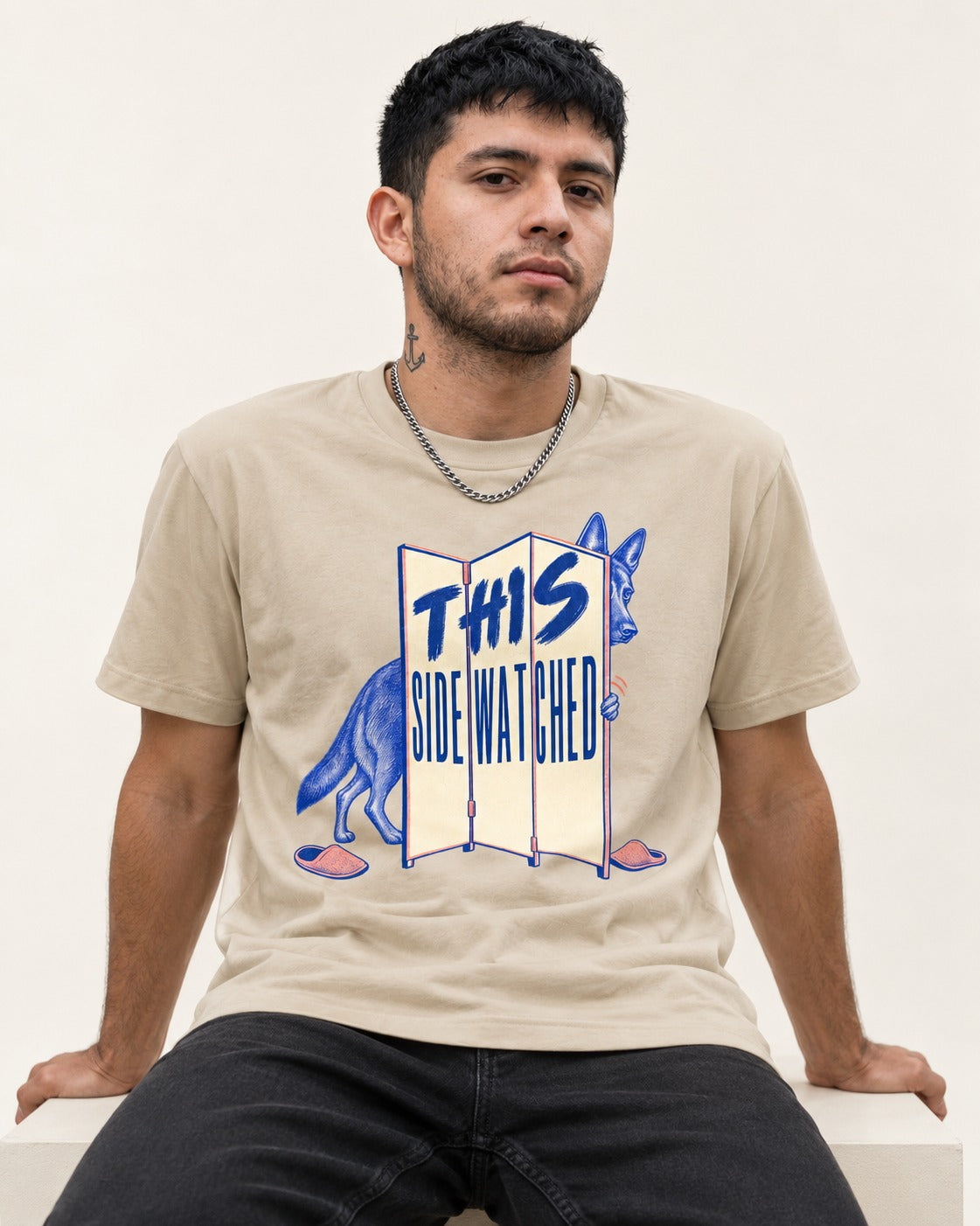 This Side Watched by German Shepherd Dog T-Shirt in Sand, worn by a seated model