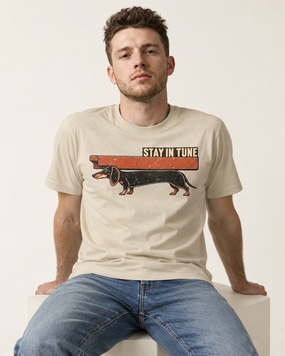 Dachshund Stay in Tune T-Shirt in Sand, worn by a seated model