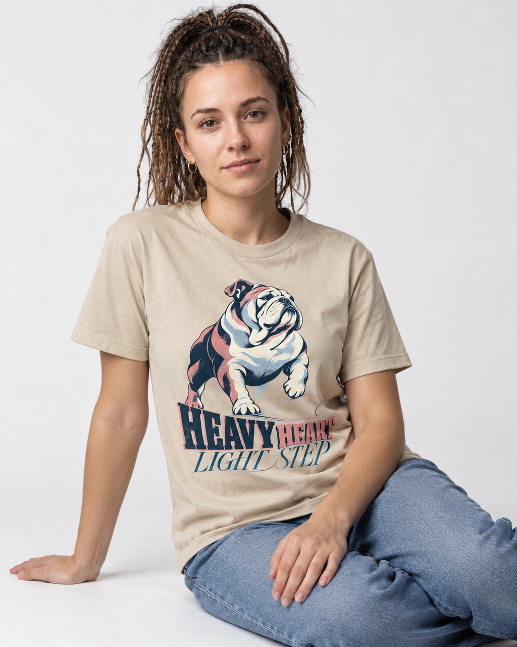 Heavy Heart Light Step English Bulldog T-Shirt in Sand, worn by a seated model