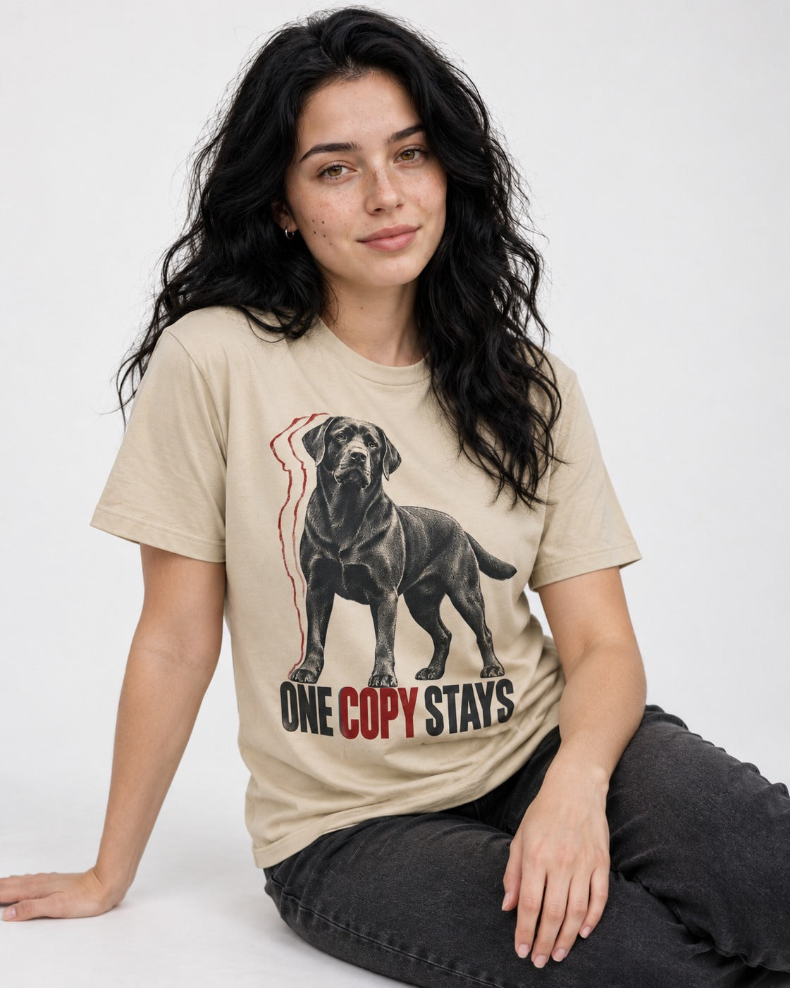 One Copy Stays Labrador Retriever T-Shirt in Sand, worn by a seated model