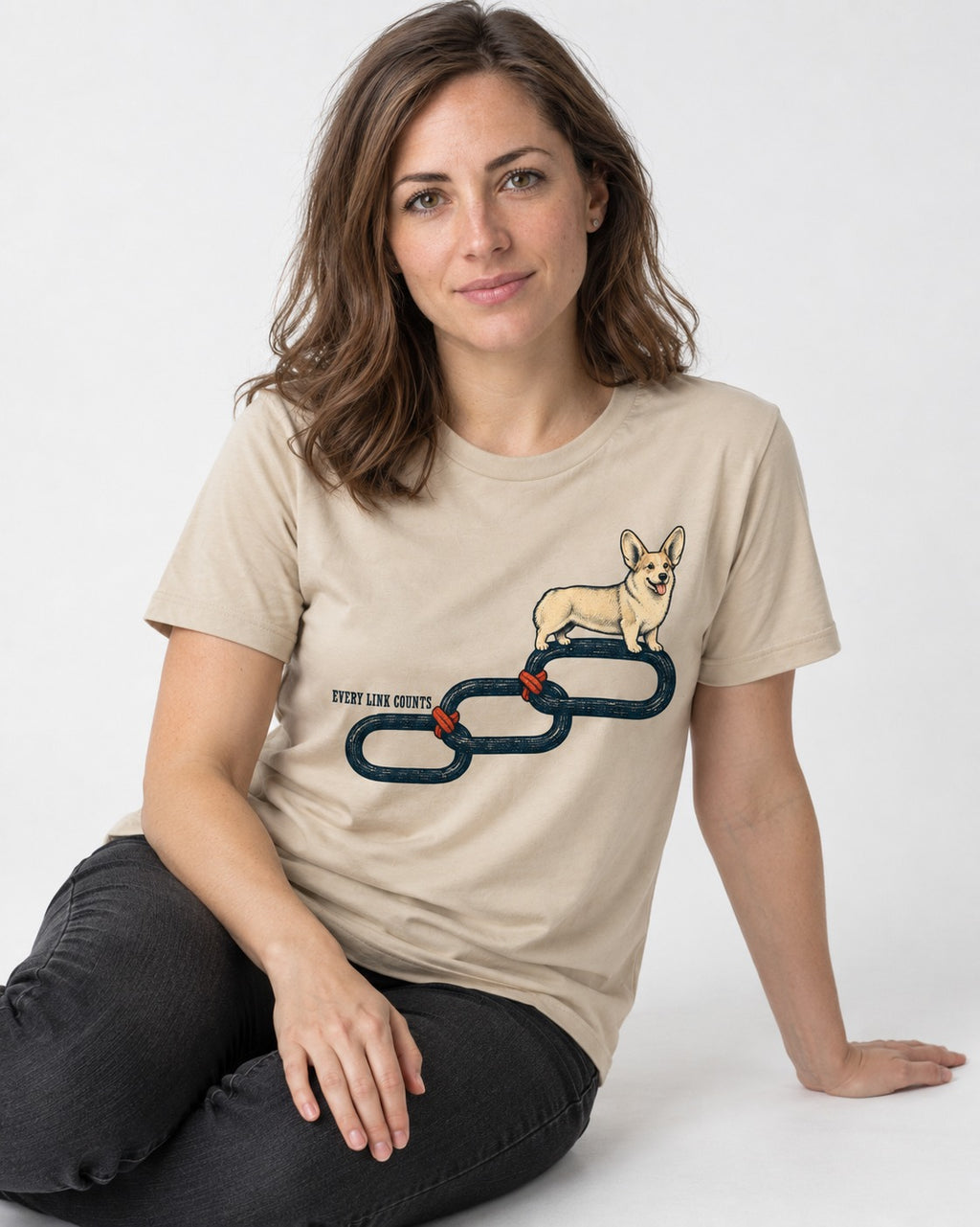 Every Corgi Link Counts T-Shirt in Sand, worn by a seated model