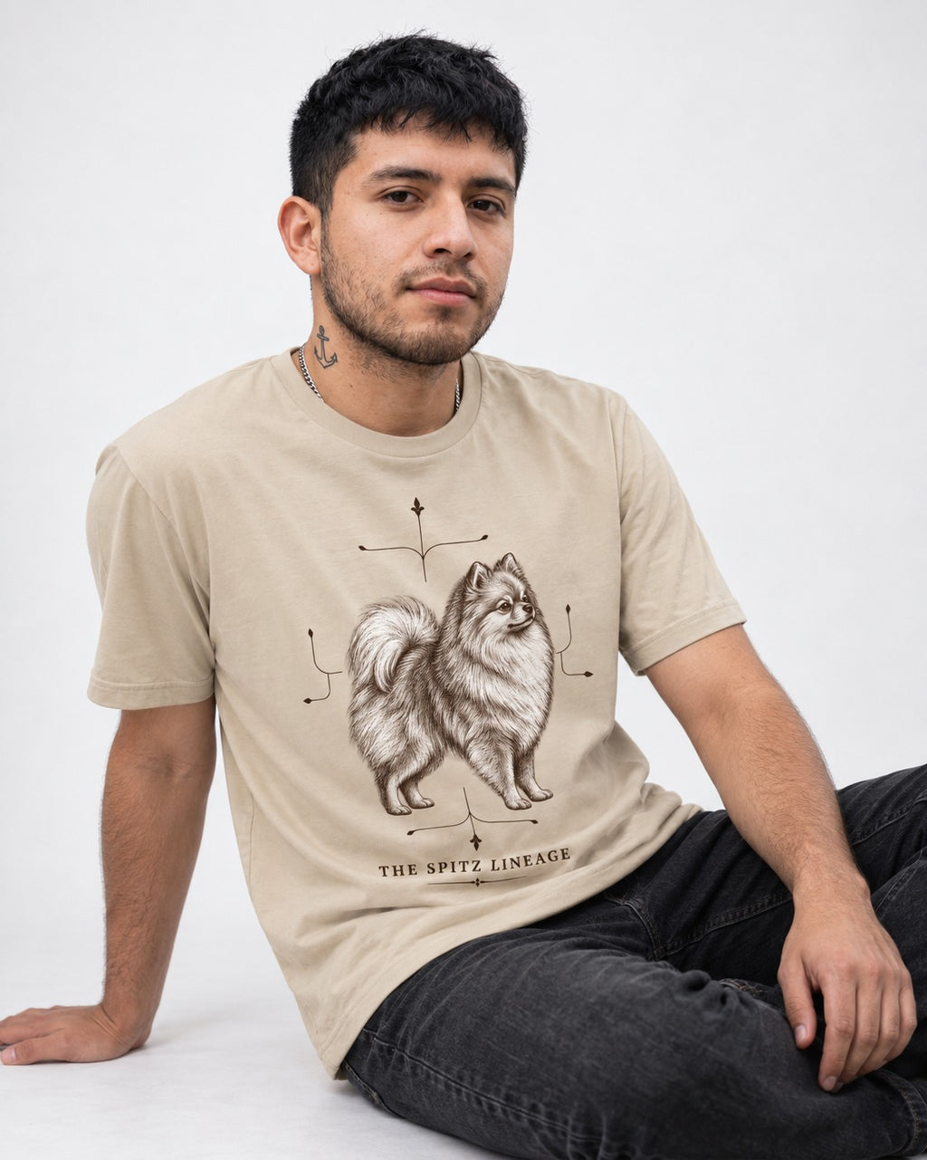 Pomeranian Spitz Lineage T-Shirt in Sand, worn by a seated model