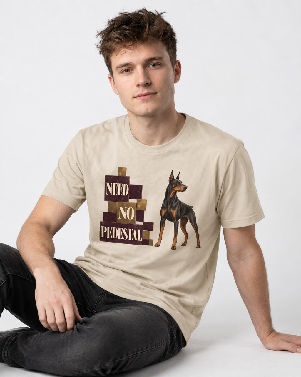 Doberman Need No Pedestal T-Shirt in Sand, worn by a seated model